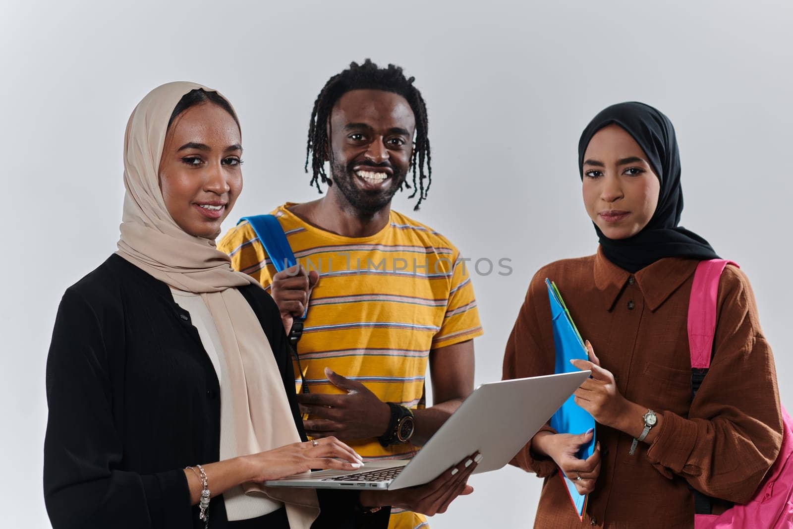 A group of students, including an African American student and two hijab-wearing women, stand united against a pristine white background, symbolizing a harmonious blend of cultures and backgrounds in the pursuit of knowledge and academic excellence.