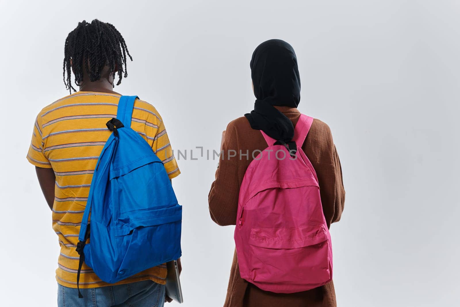 African American student collaborates with his Muslim colleague, who diligently works on her laptop, symbolizing a blend of diversity, modern learning, and cooperative spirit against a serene white background by dotshock
