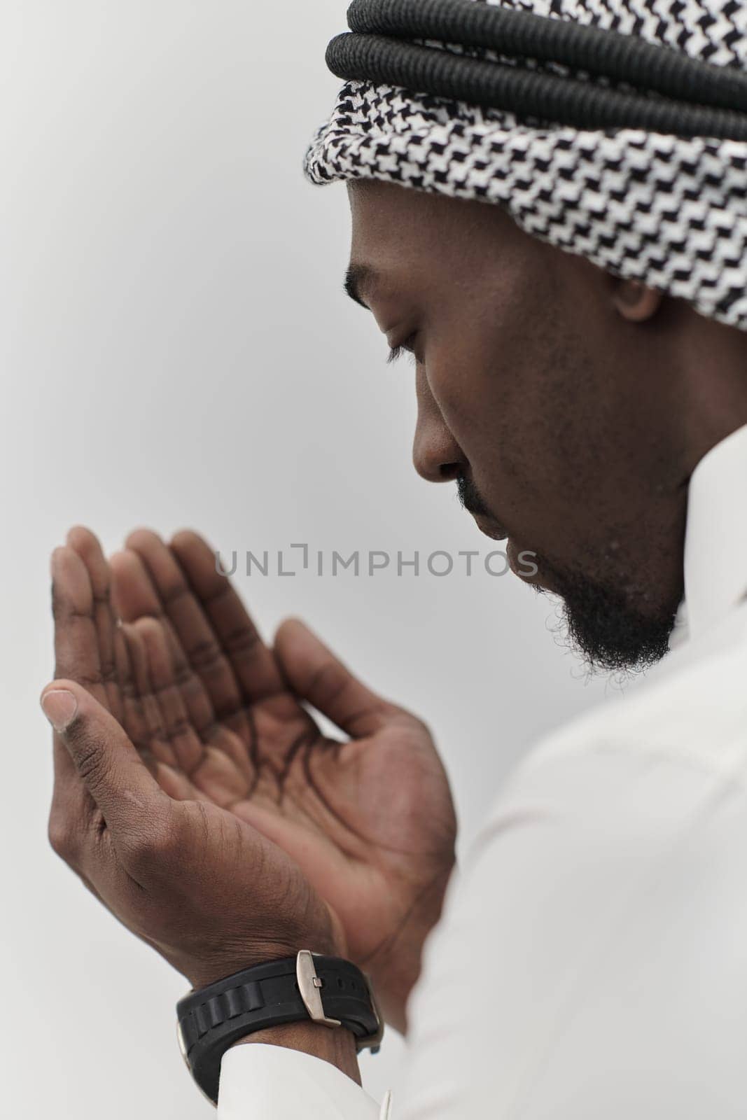 African American Muslim man raises his hands in prayer, seeking solace and devotion to God, as he stands isolated against a serene white backdrop, symbolizing a profound expression of faith and contemplation.