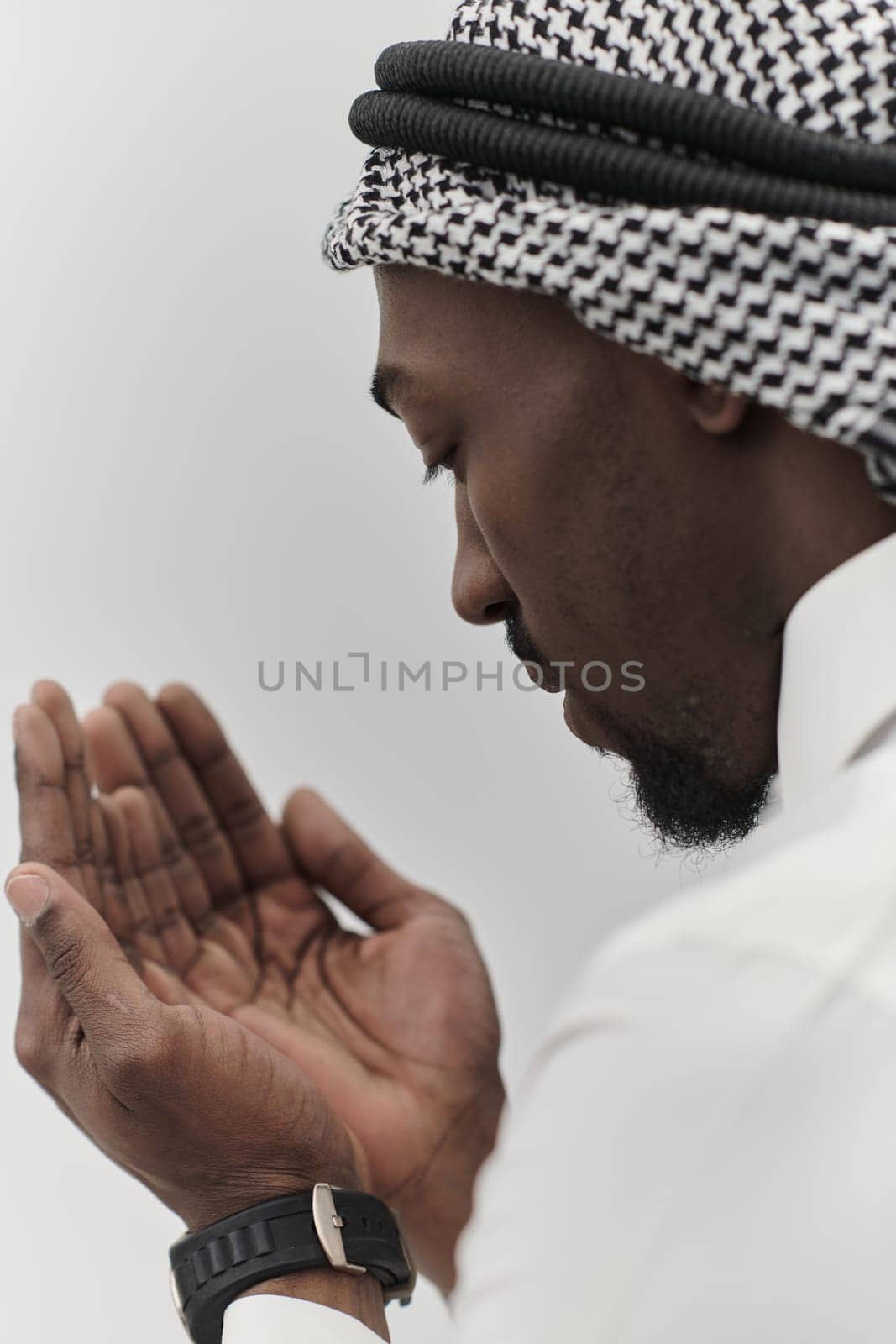 African American Muslim man raises his hands in prayer, seeking solace and devotion to God, as he stands isolated against a serene white backdrop, symbolizing a profound expression of faith and contemplation by dotshock