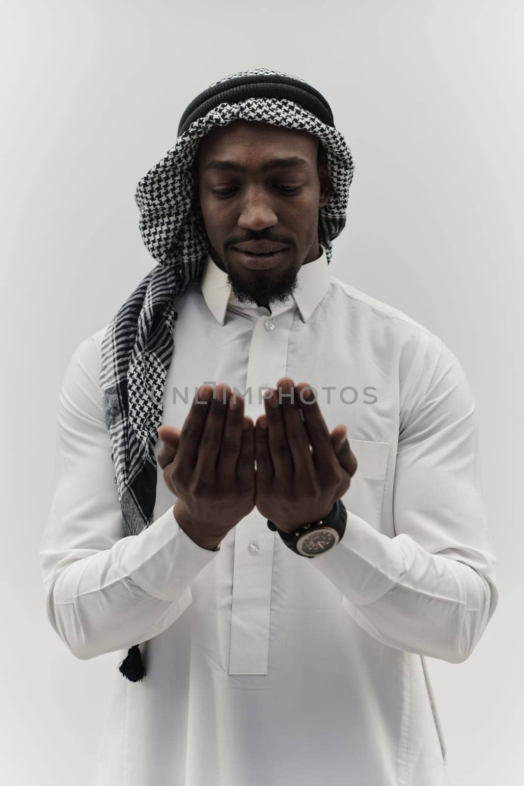 African American Muslim man raises his hands in prayer, seeking solace and devotion to God, as he stands isolated against a serene white backdrop, symbolizing a profound expression of faith and contemplation.