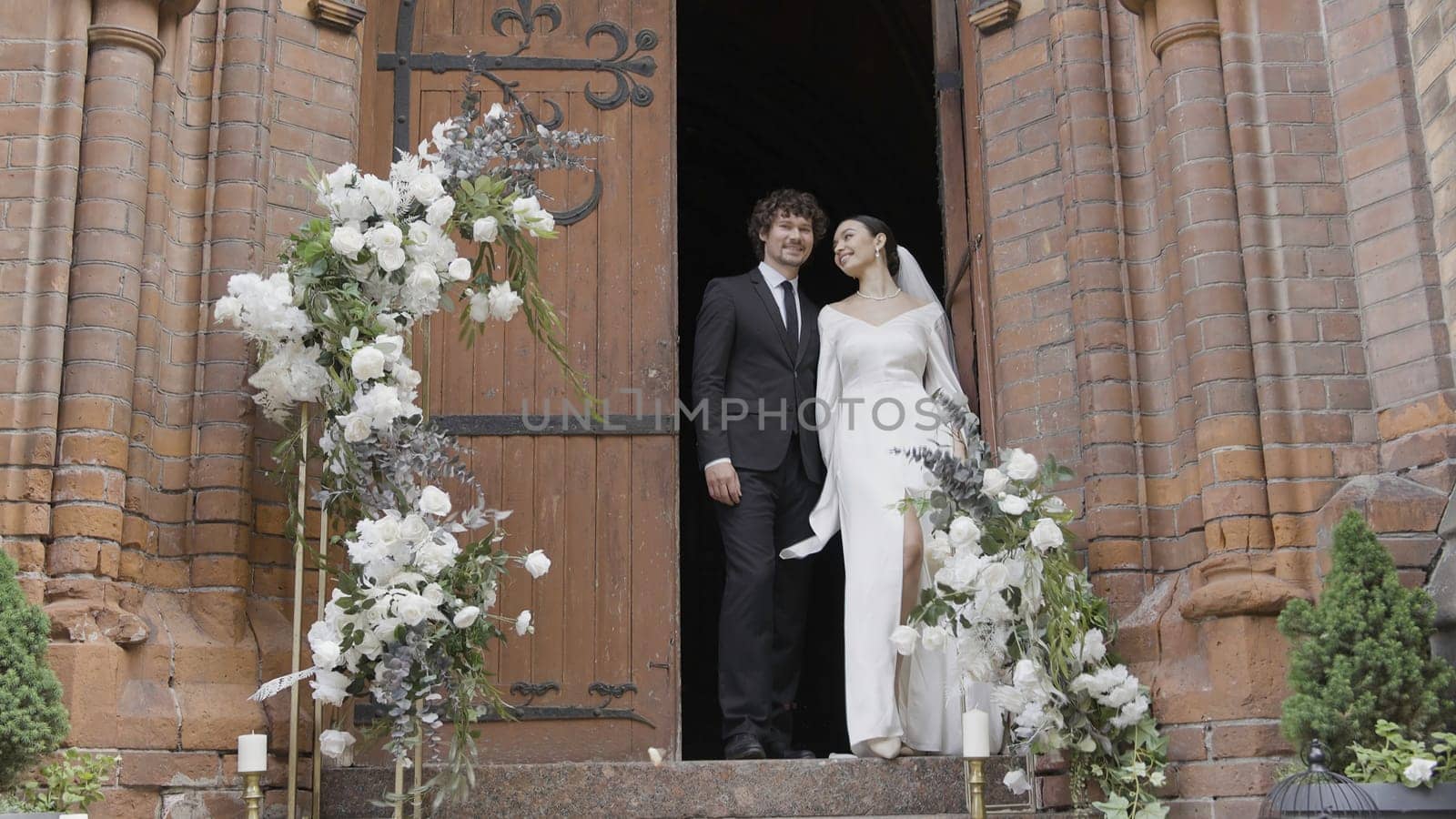Newlyweds are standing at temple. Action. Beautiful couple of newlyweds stands in doorway of temple. Newlyweds at wedding ceremony at European temple by Mediawhalestock