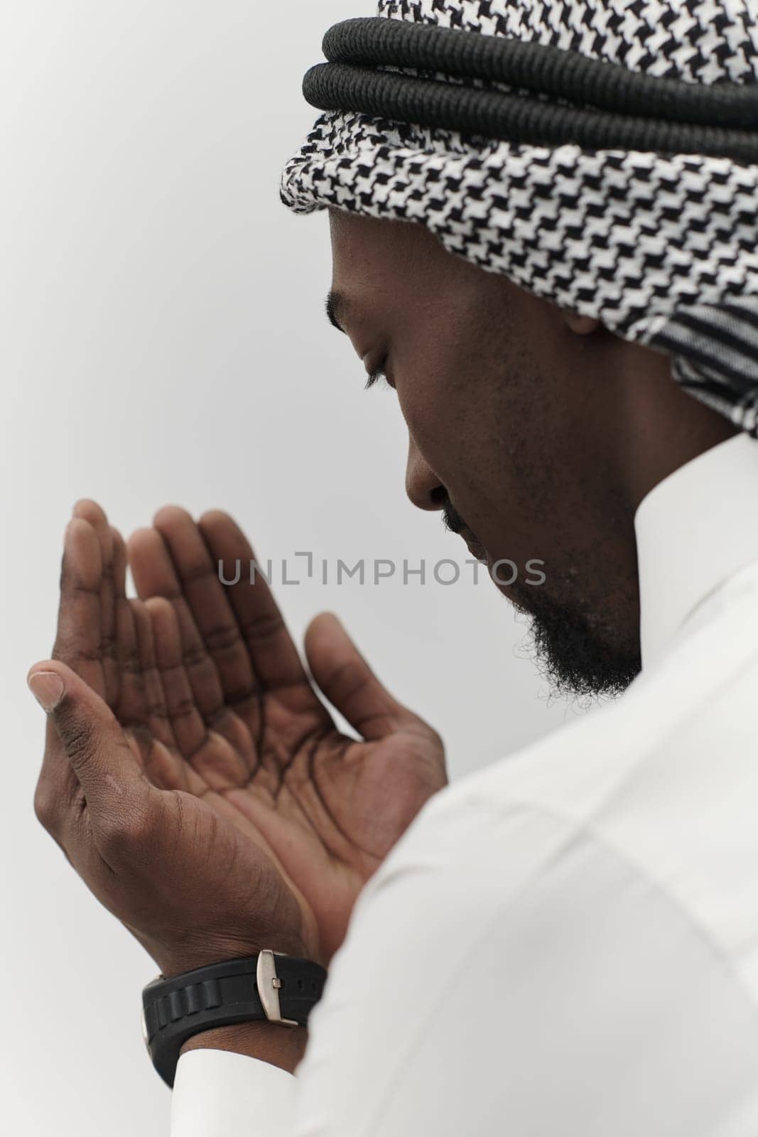 African American Muslim man raises his hands in prayer, seeking solace and devotion to God, as he stands isolated against a serene white backdrop, symbolizing a profound expression of faith and contemplation by dotshock