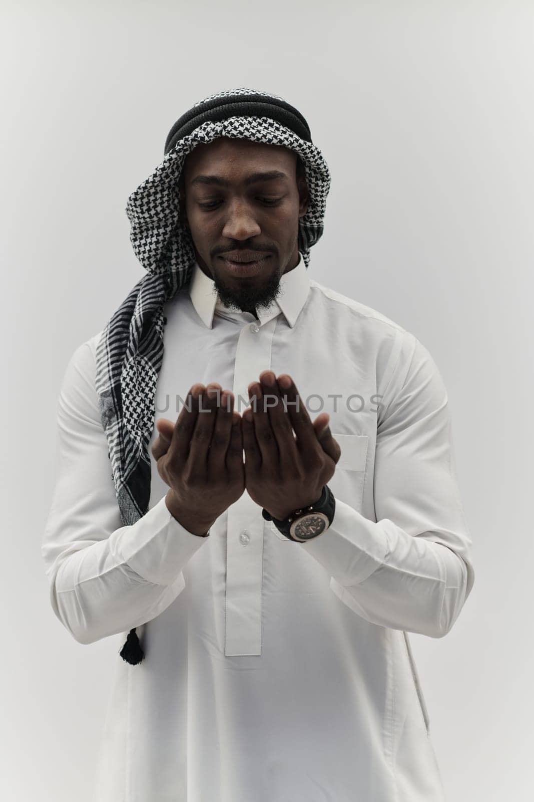 African American Muslim man raises his hands in prayer, seeking solace and devotion to God, as he stands isolated against a serene white backdrop, symbolizing a profound expression of faith and contemplation by dotshock