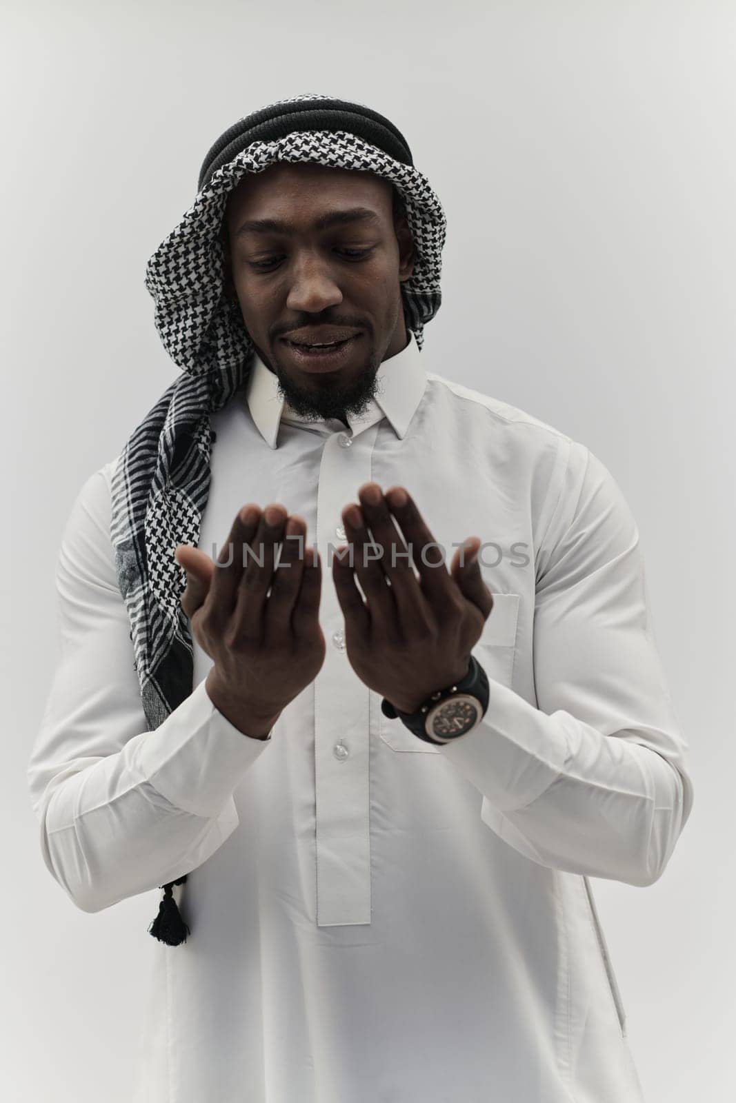 African American Muslim man raises his hands in prayer, seeking solace and devotion to God, as he stands isolated against a serene white backdrop, symbolizing a profound expression of faith and contemplation by dotshock