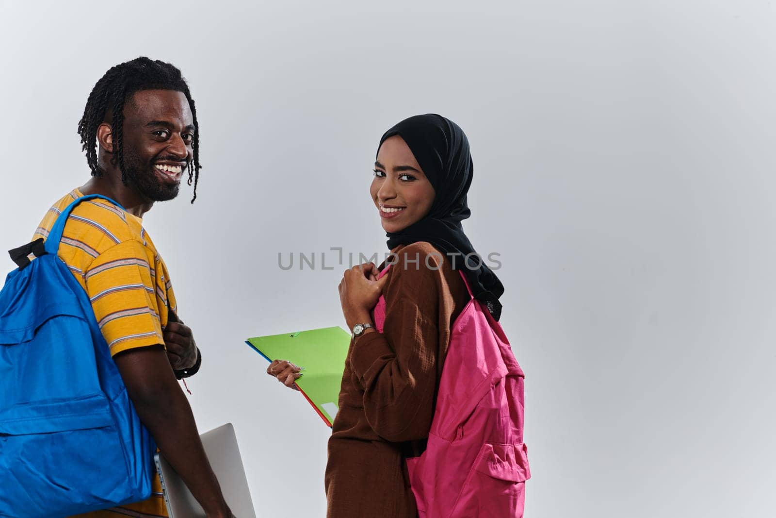 African American student collaborates with his Muslim colleague, who diligently works on her laptop, symbolizing a blend of diversity, modern learning, and cooperative spirit against a serene white background by dotshock