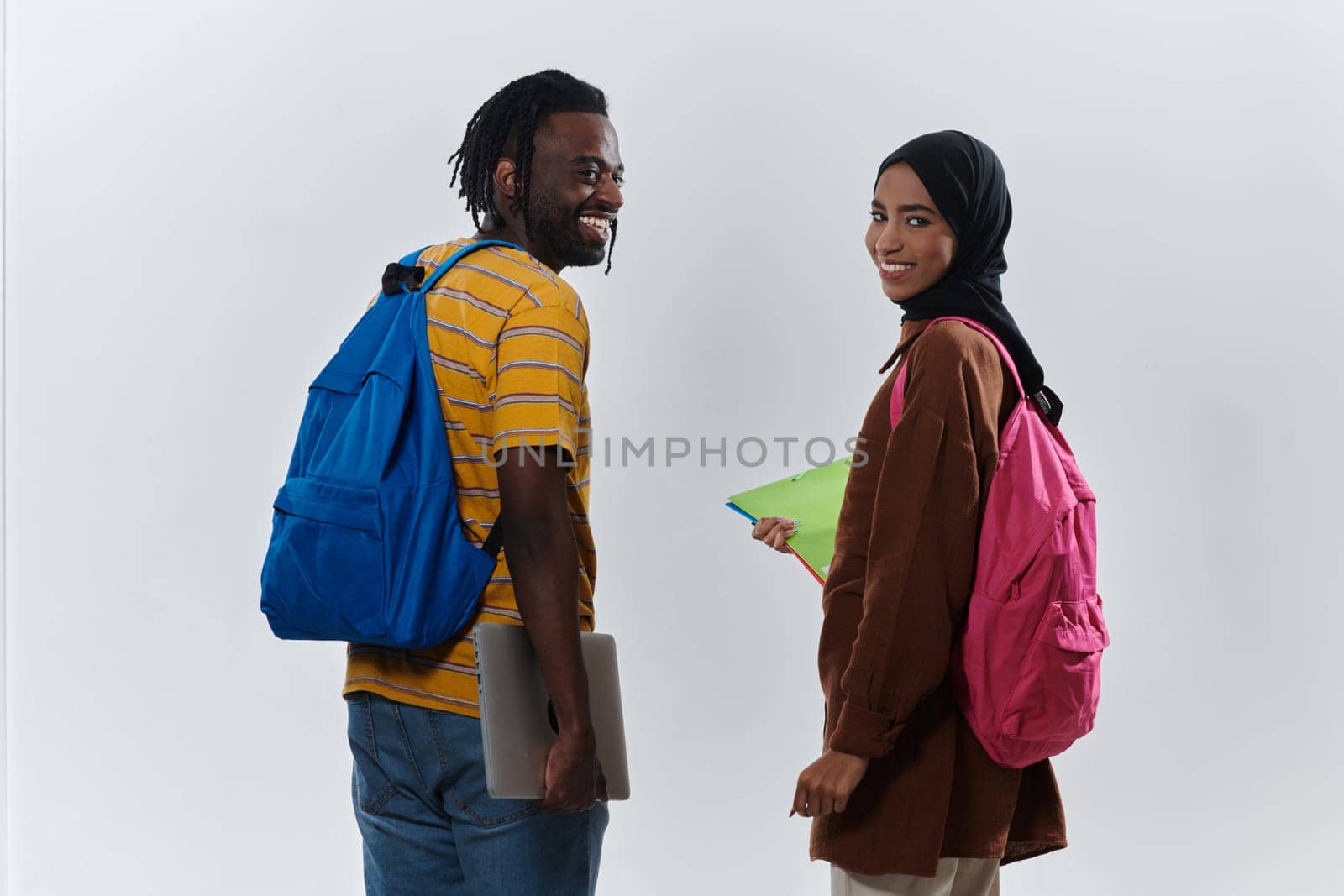 African American student collaborates with his Muslim colleague, who diligently works on her laptop, symbolizing a blend of diversity, modern learning, and cooperative spirit against a serene white background.