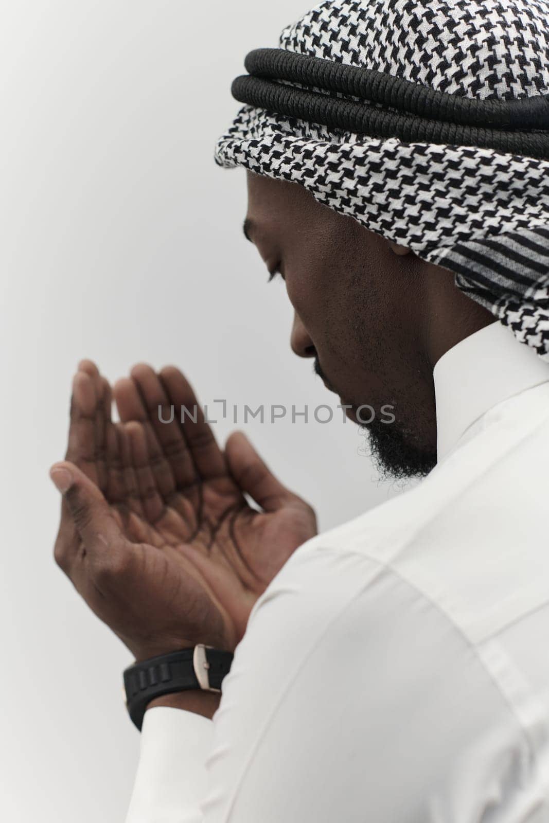 African American Muslim man raises his hands in prayer, seeking solace and devotion to God, as he stands isolated against a serene white backdrop, symbolizing a profound expression of faith and contemplation.