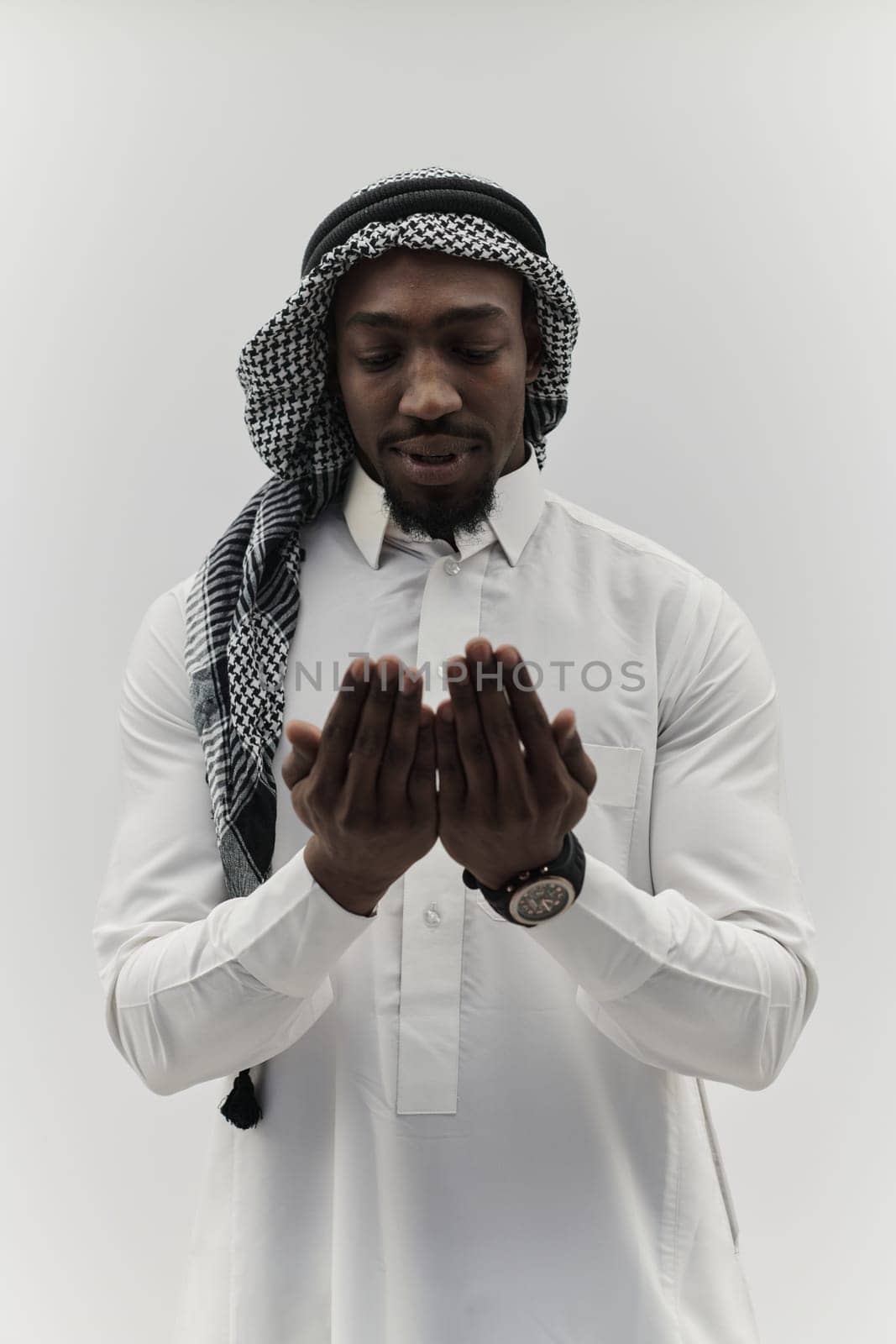 African American Muslim man raises his hands in prayer, seeking solace and devotion to God, as he stands isolated against a serene white backdrop, symbolizing a profound expression of faith and contemplation by dotshock