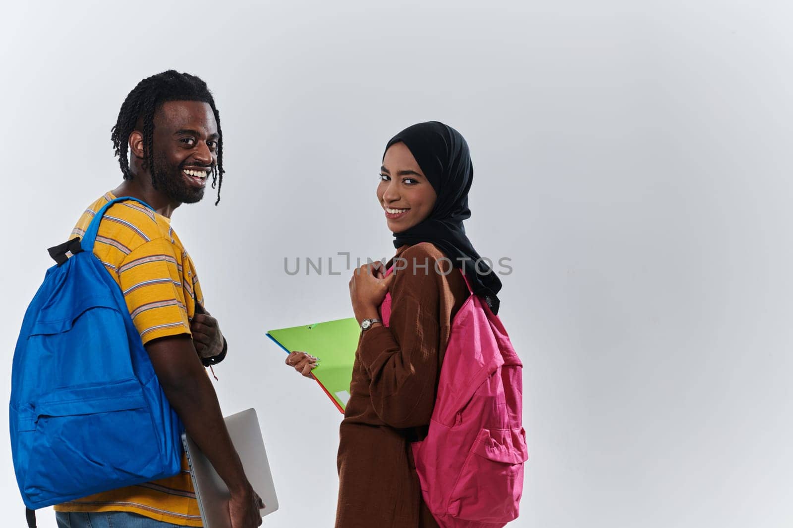 African American student collaborates with his Muslim colleague, who diligently works on her laptop, symbolizing a blend of diversity, modern learning, and cooperative spirit against a serene white background.