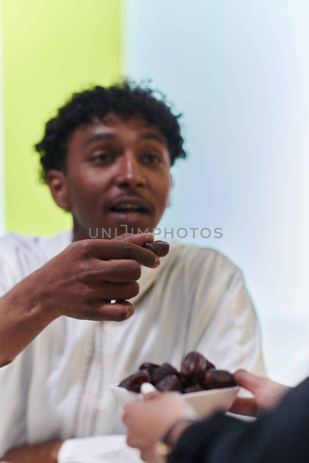 African American Muslim man delicately takes dates to break his fast during the Ramadan month, seated at the family dinner table, embodying a scene of spiritual reflection, cultural tradition, and the shared anticipation of the communal iftar.