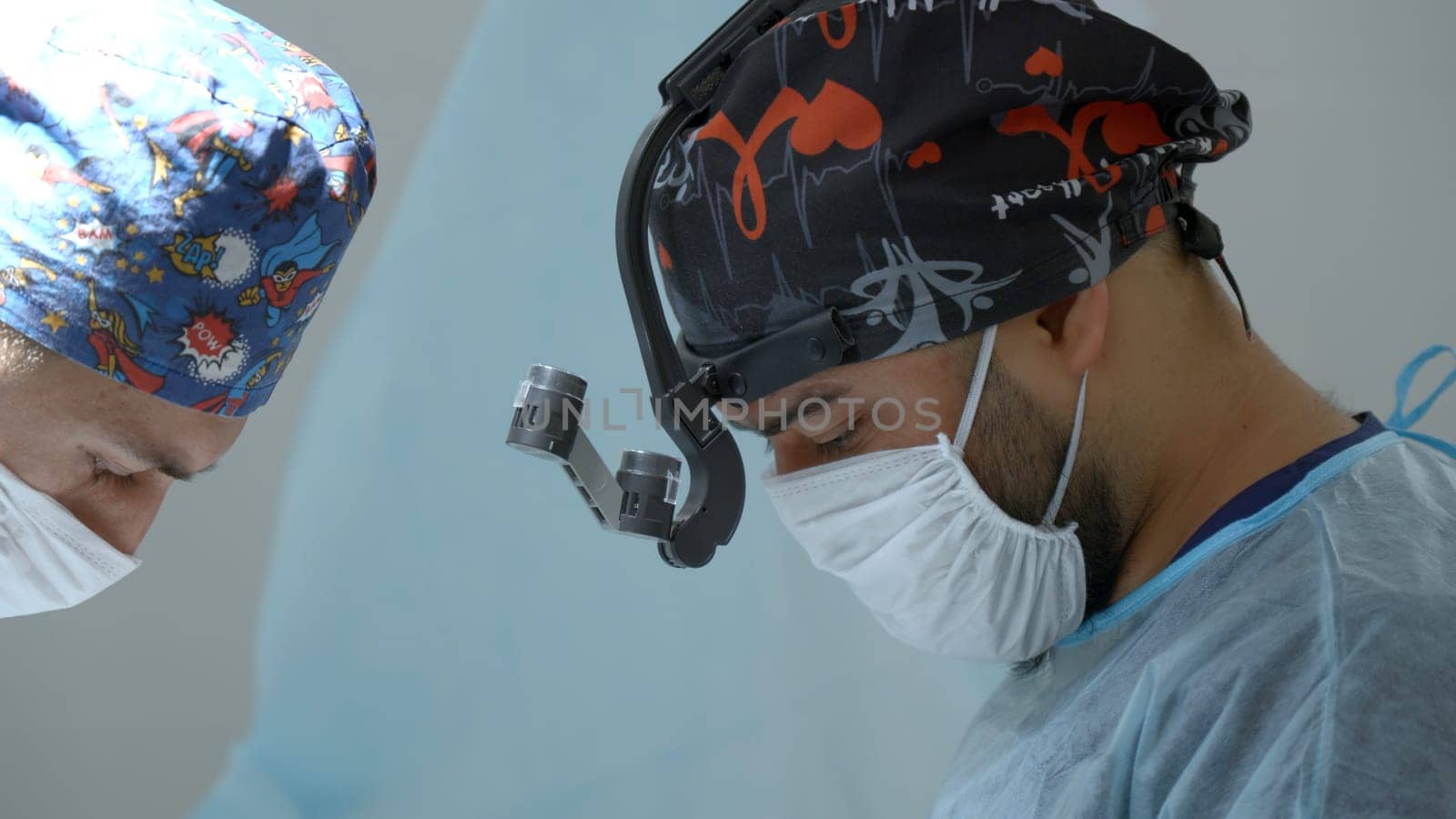 Close up of male doctors heads in sterile uniform and mask. Action. Surgeon with binocular loupe, professional medical equipment