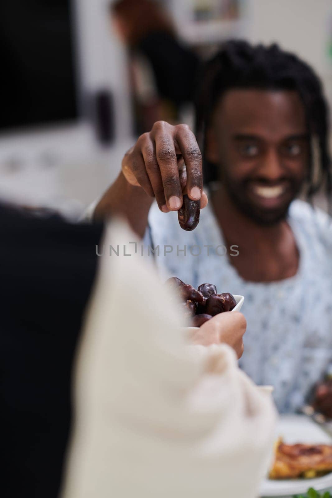 African American Muslim man delicately takes dates to break his fast during the Ramadan month, seated at the family dinner table, embodying a scene of spiritual reflection, cultural tradition, and the shared anticipation of the communal iftar by dotshock