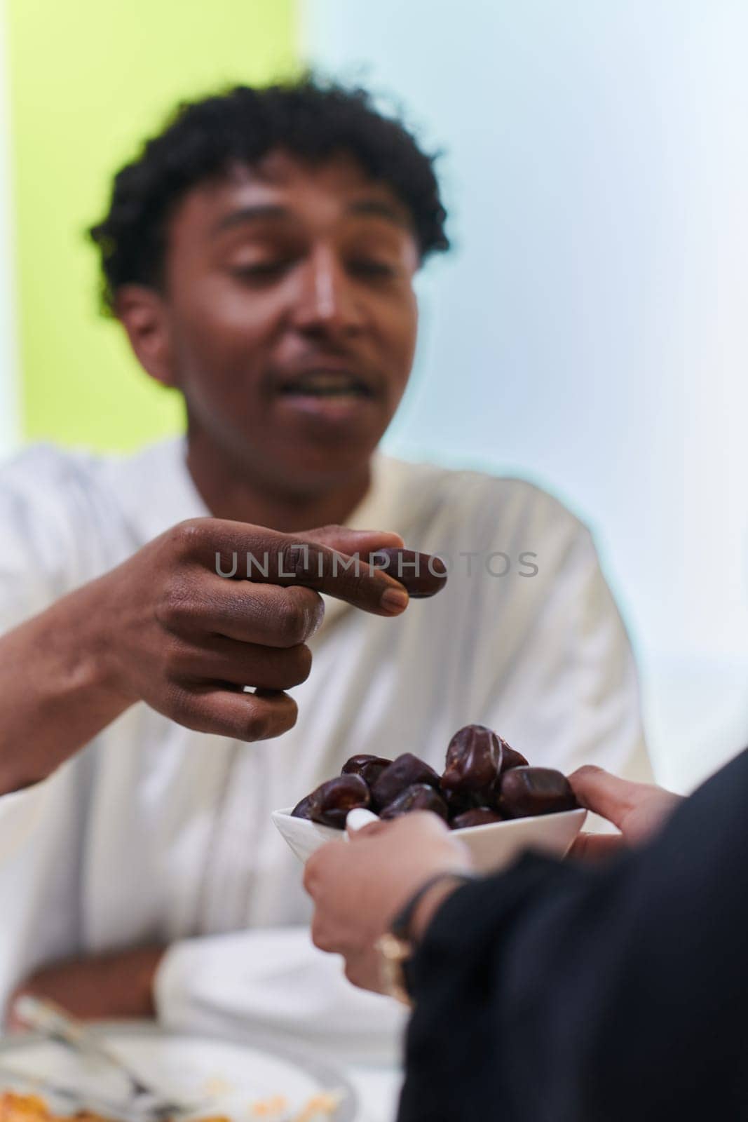 African American Muslim man delicately takes dates to break his fast during the Ramadan month, seated at the family dinner table, embodying a scene of spiritual reflection, cultural tradition, and the shared anticipation of the communal iftar by dotshock