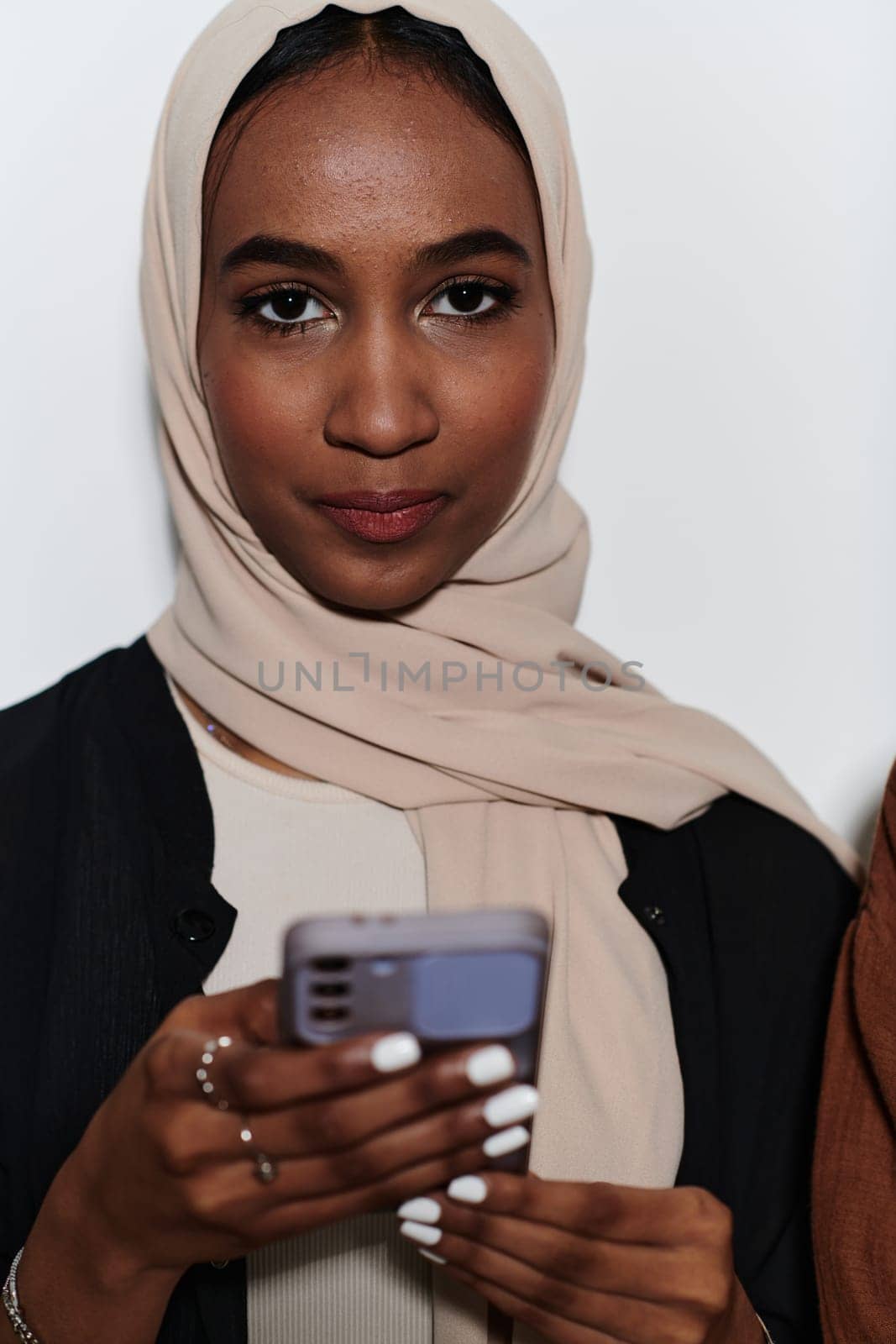 An elegant Arab woman, adorned in a hijab, engages with modernity as she uses a smartphone, the juxtaposition of traditional attire against contemporary technology captured in the isolated setting against a pristine white background.