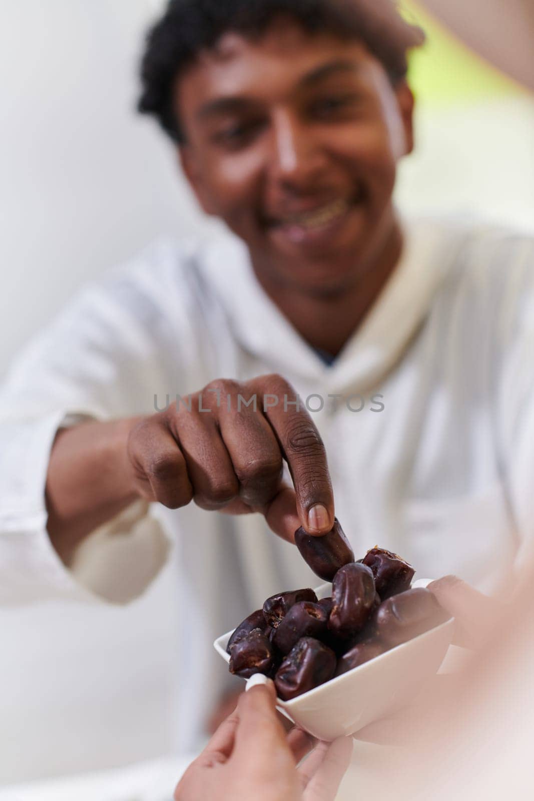 African American Muslim man delicately takes dates to break his fast during the Ramadan month, seated at the family dinner table, embodying a scene of spiritual reflection, cultural tradition, and the shared anticipation of the communal iftar by dotshock