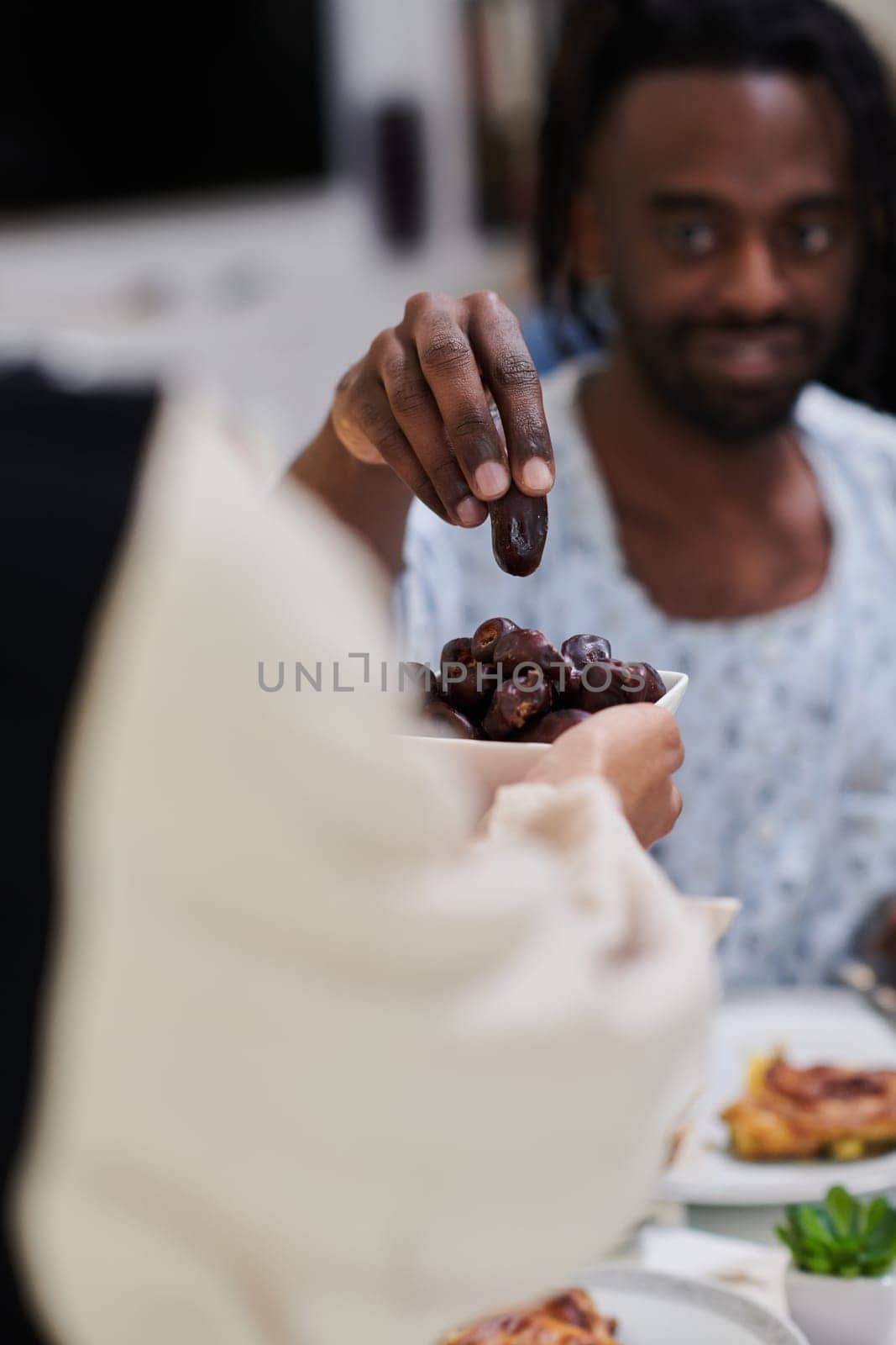 African American Muslim man delicately takes dates to break his fast during the Ramadan month, seated at the family dinner table, embodying a scene of spiritual reflection, cultural tradition, and the shared anticipation of the communal iftar.