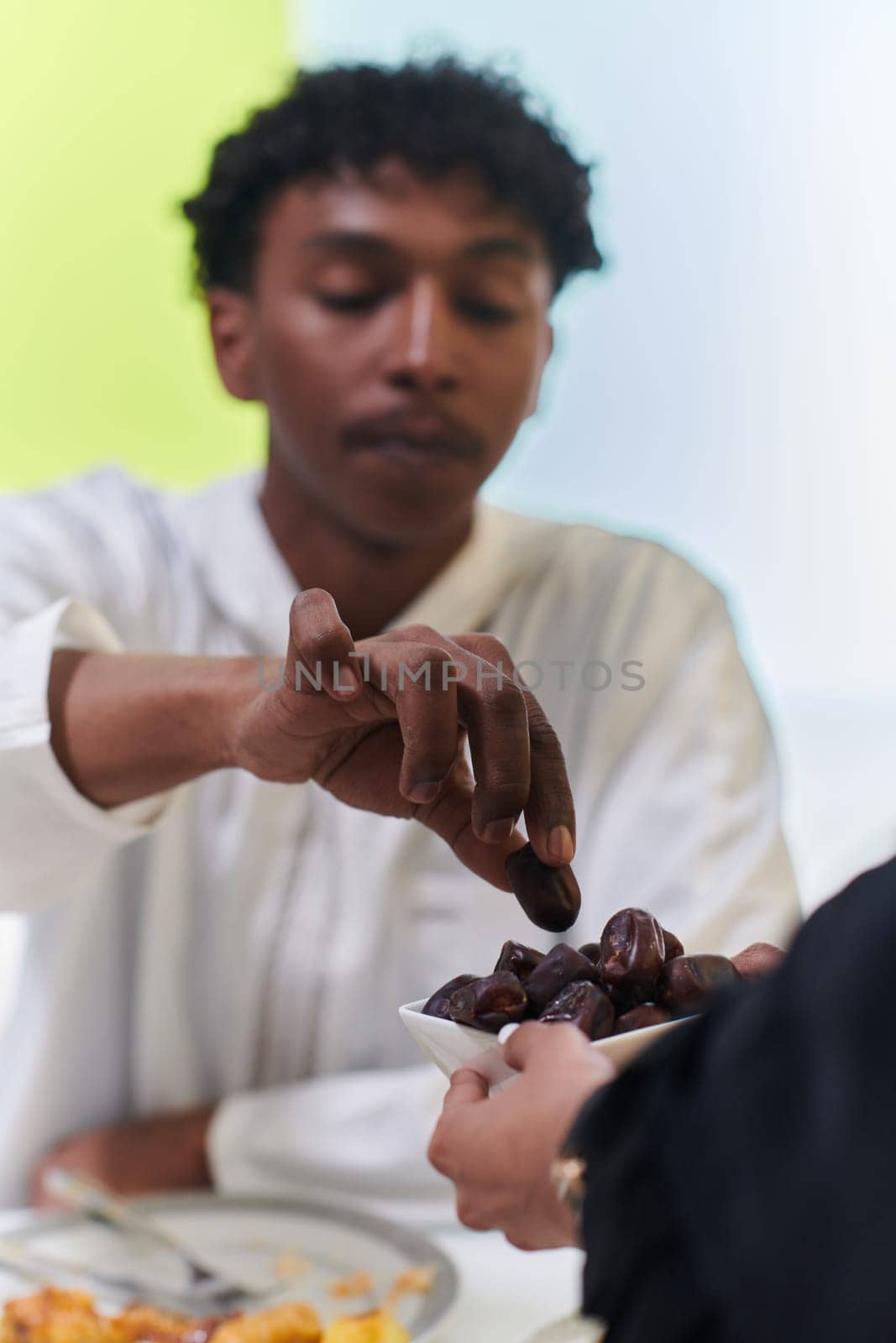 African American Muslim man delicately takes dates to break his fast during the Ramadan month, seated at the family dinner table, embodying a scene of spiritual reflection, cultural tradition, and the shared anticipation of the communal iftar by dotshock