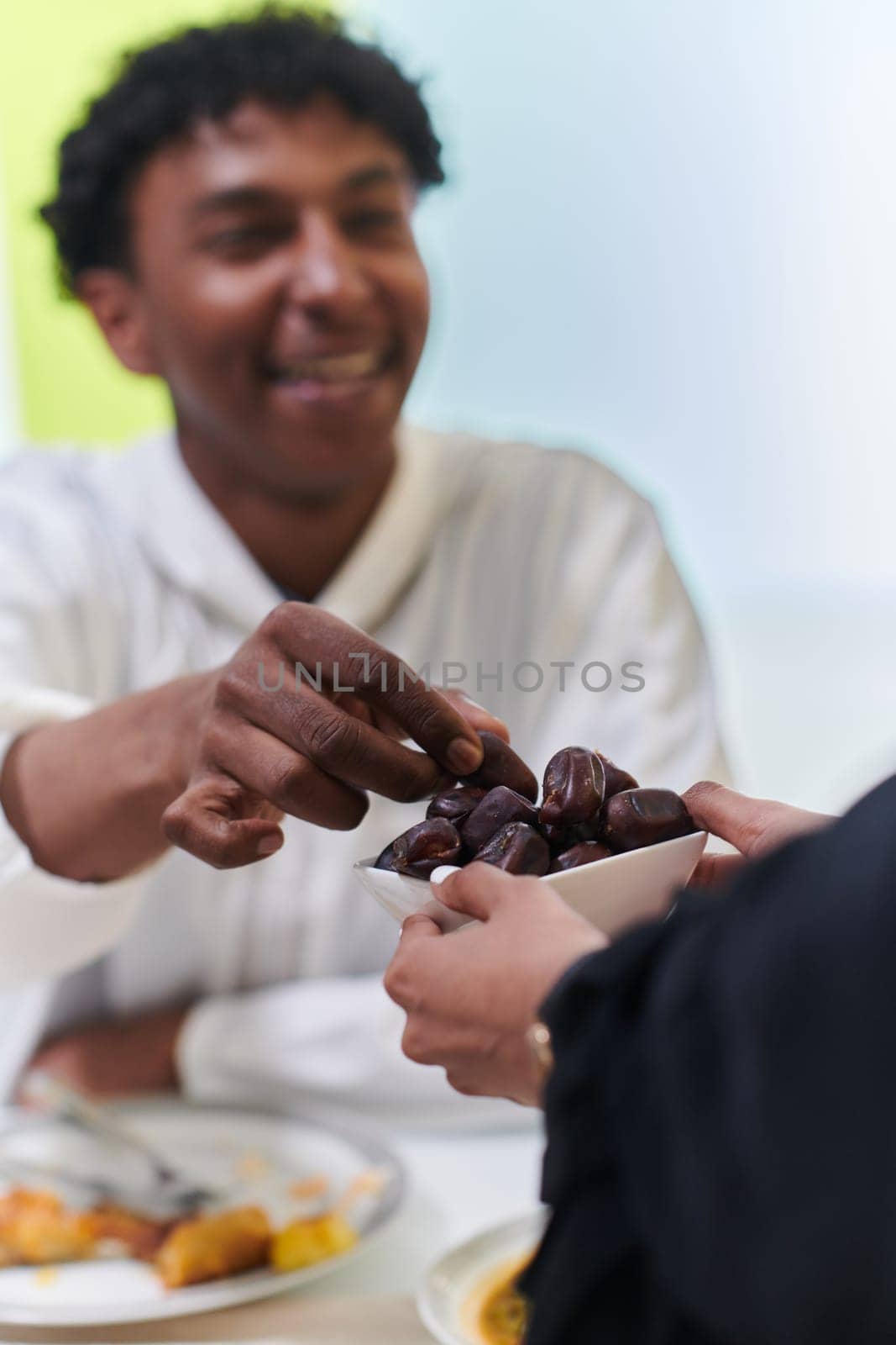 African American Muslim man delicately takes dates to break his fast during the Ramadan month, seated at the family dinner table, embodying a scene of spiritual reflection, cultural tradition, and the shared anticipation of the communal iftar by dotshock