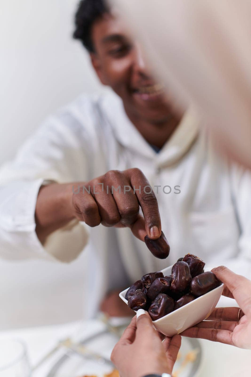 African American Muslim man delicately takes dates to break his fast during the Ramadan month, seated at the family dinner table, embodying a scene of spiritual reflection, cultural tradition, and the shared anticipation of the communal iftar by dotshock