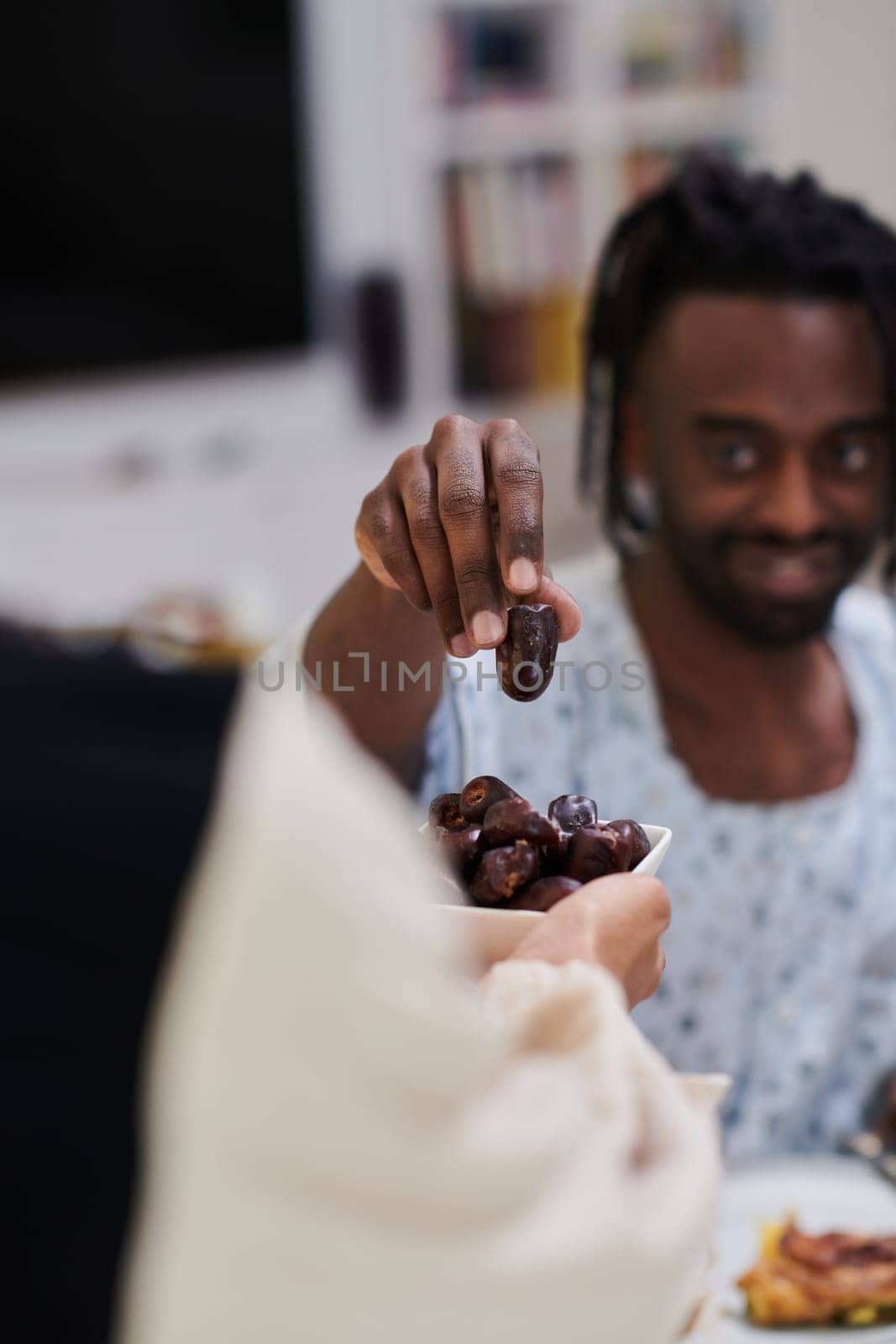 African American Muslim man delicately takes dates to break his fast during the Ramadan month, seated at the family dinner table, embodying a scene of spiritual reflection, cultural tradition, and the shared anticipation of the communal iftar.