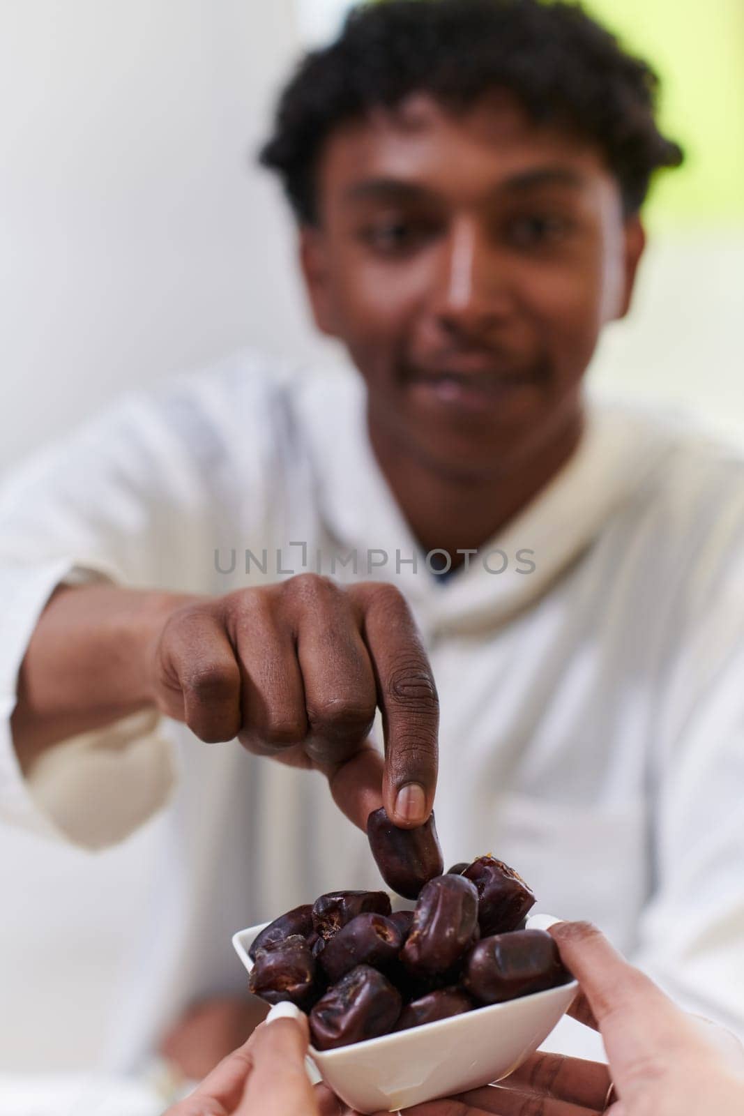 African American Muslim man delicately takes dates to break his fast during the Ramadan month, seated at the family dinner table, embodying a scene of spiritual reflection, cultural tradition, and the shared anticipation of the communal iftar by dotshock