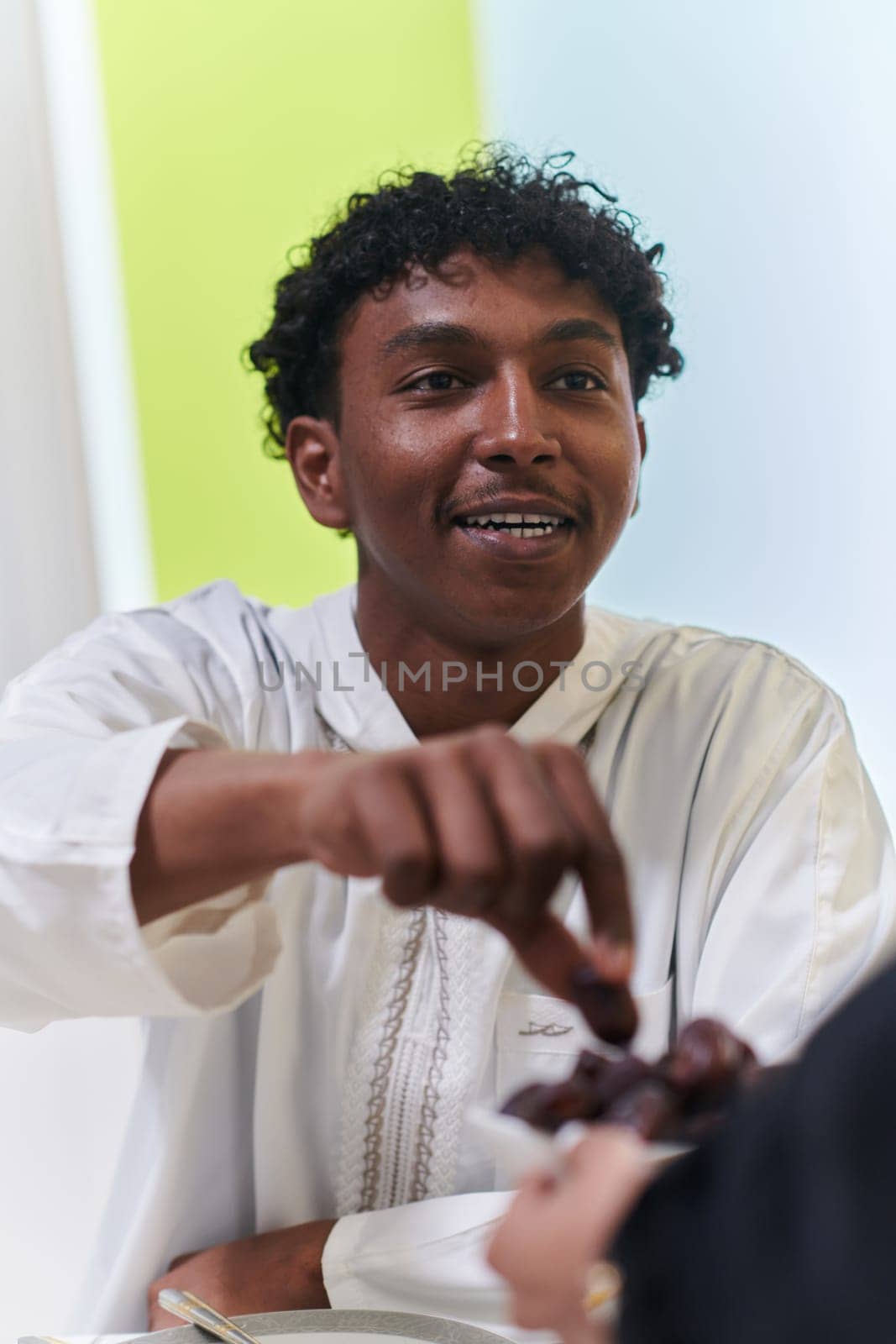 African American Muslim man delicately takes dates to break his fast during the Ramadan month, seated at the family dinner table, embodying a scene of spiritual reflection, cultural tradition, and the shared anticipation of the communal iftar.