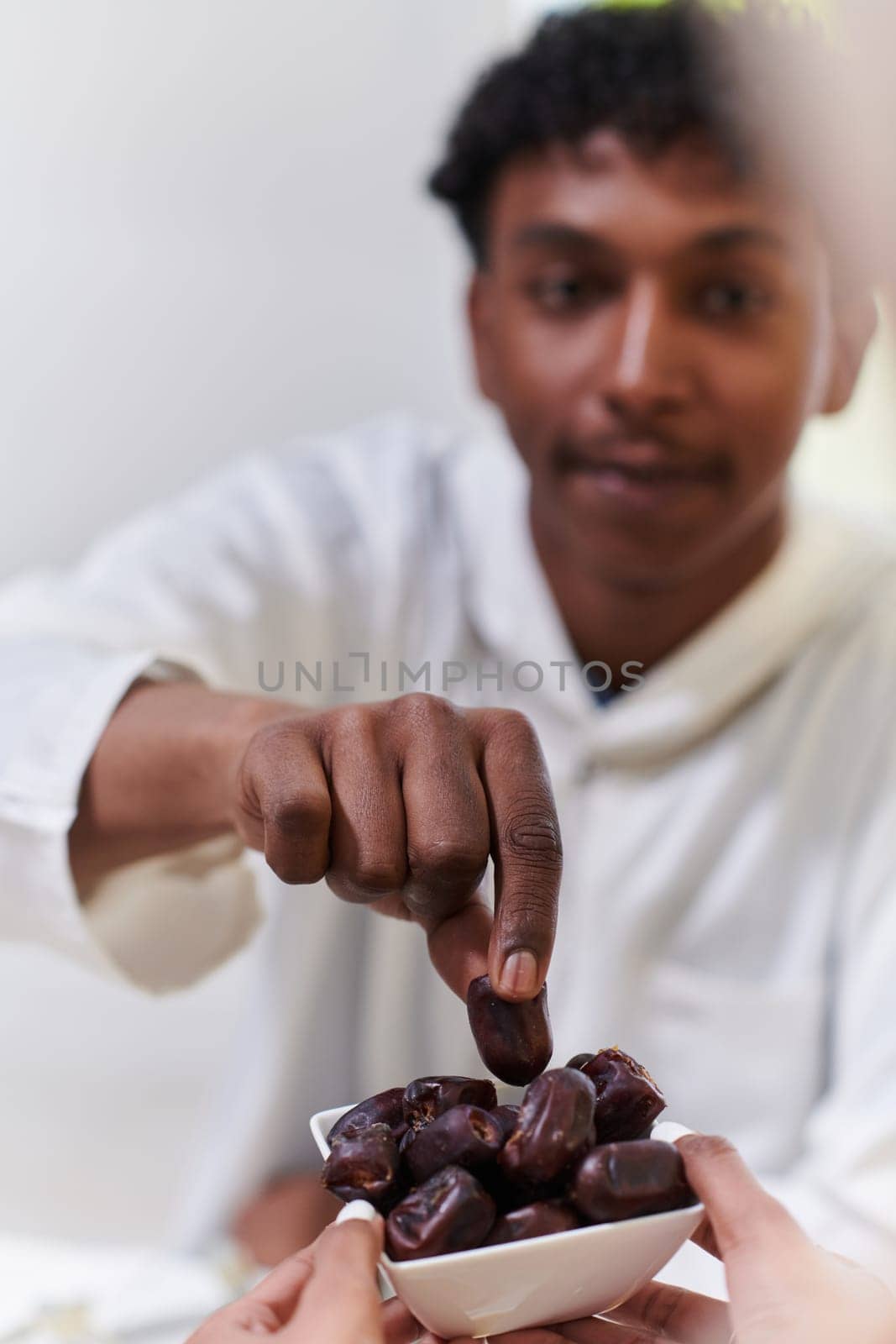 African American Muslim man delicately takes dates to break his fast during the Ramadan month, seated at the family dinner table, embodying a scene of spiritual reflection, cultural tradition, and the shared anticipation of the communal iftar by dotshock