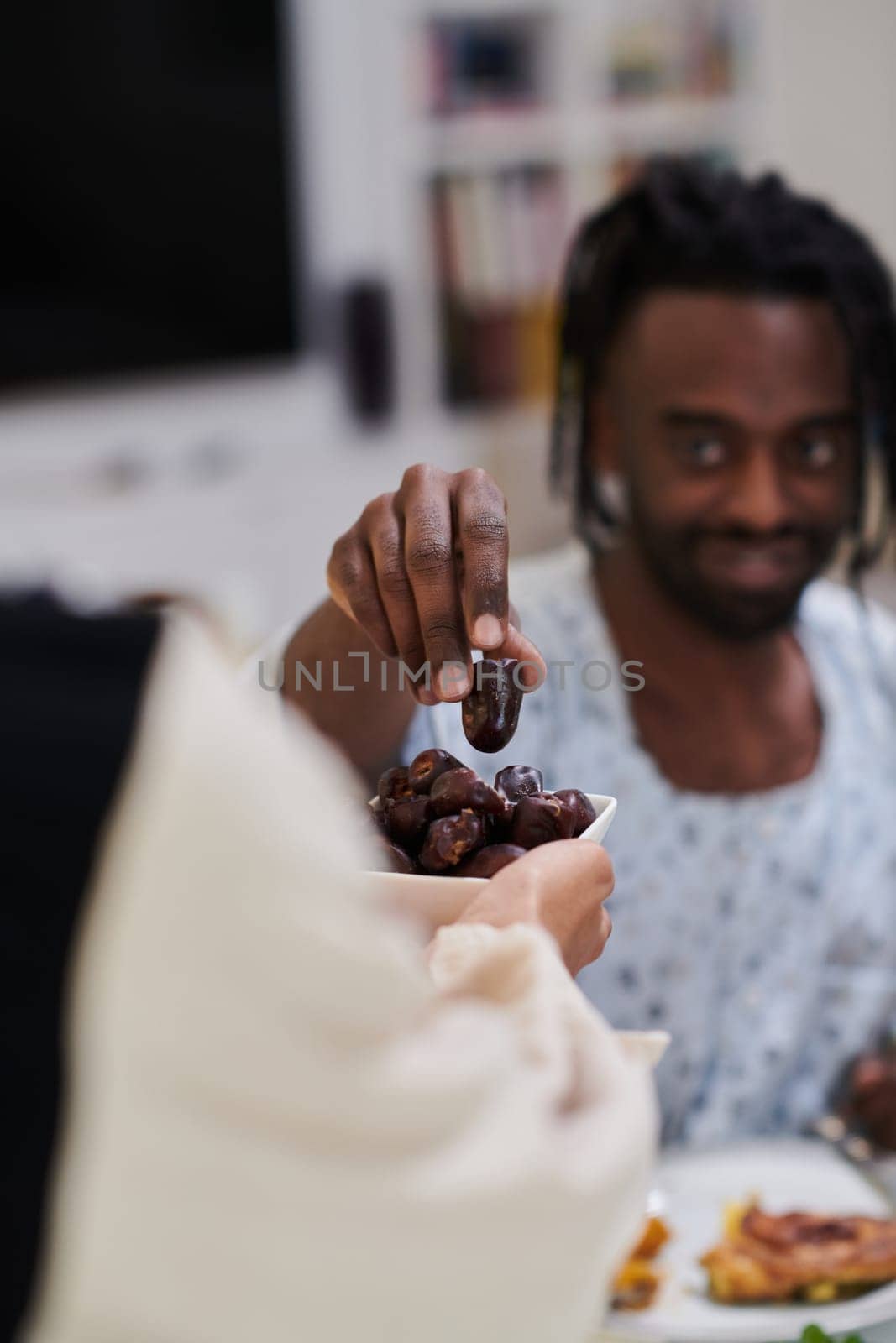 African American Muslim man delicately takes dates to break his fast during the Ramadan month, seated at the family dinner table, embodying a scene of spiritual reflection, cultural tradition, and the shared anticipation of the communal iftar by dotshock