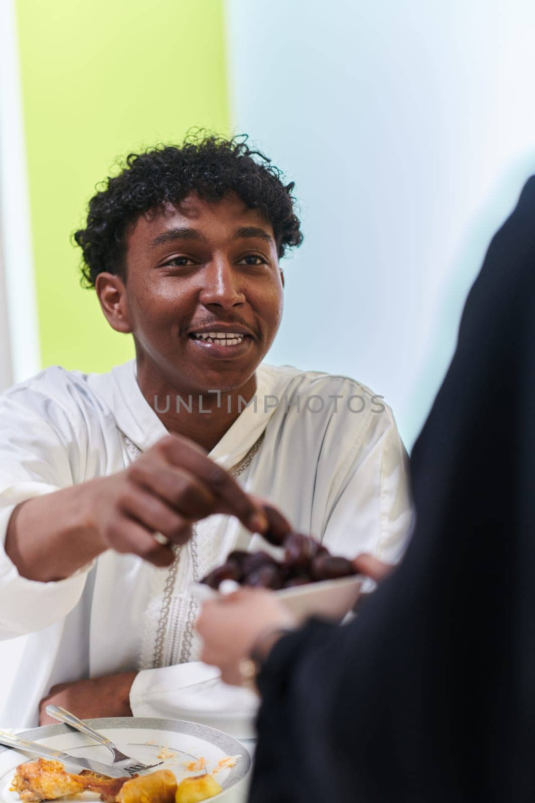 African American Muslim man delicately takes dates to break his fast during the Ramadan month, seated at the family dinner table, embodying a scene of spiritual reflection, cultural tradition, and the shared anticipation of the communal iftar.