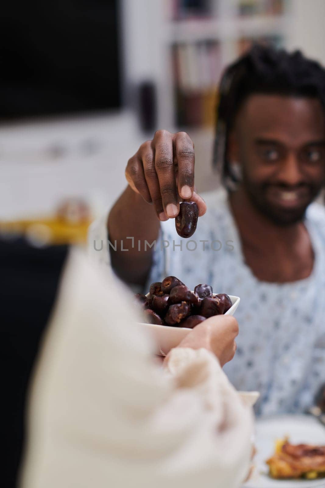 African American Muslim man delicately takes dates to break his fast during the Ramadan month, seated at the family dinner table, embodying a scene of spiritual reflection, cultural tradition, and the shared anticipation of the communal iftar by dotshock