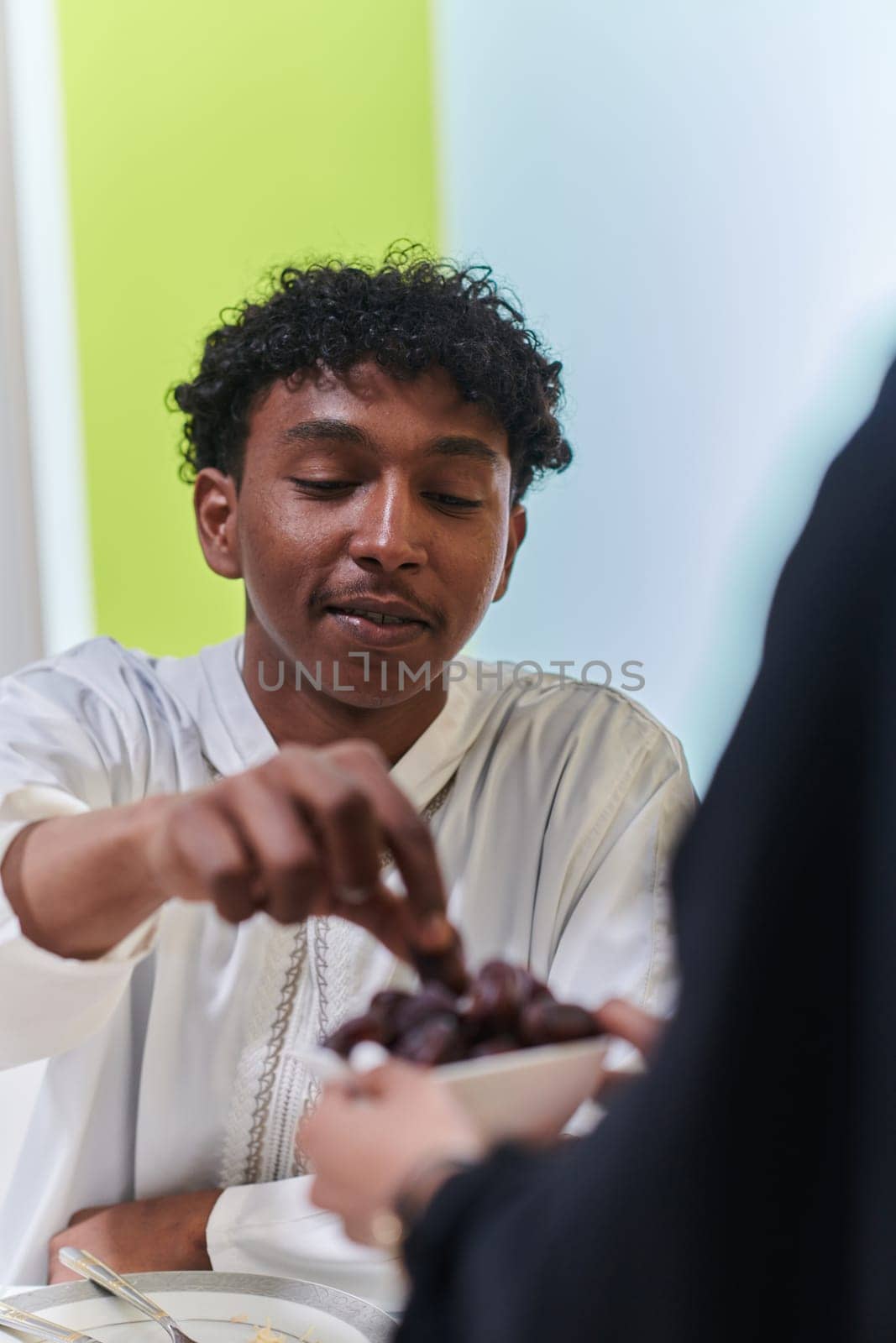 African American Muslim man delicately takes dates to break his fast during the Ramadan month, seated at the family dinner table, embodying a scene of spiritual reflection, cultural tradition, and the shared anticipation of the communal iftar by dotshock