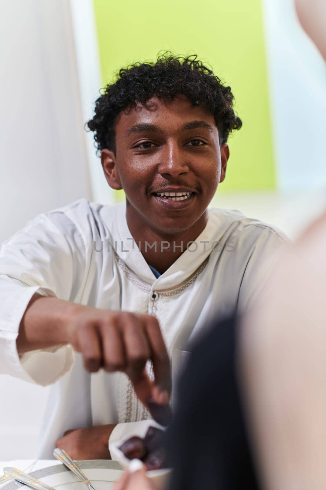 African American Muslim man delicately takes dates to break his fast during the Ramadan month, seated at the family dinner table, embodying a scene of spiritual reflection, cultural tradition, and the shared anticipation of the communal iftar by dotshock