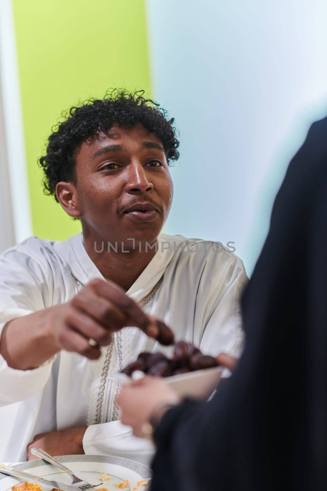 African American Muslim man delicately takes dates to break his fast during the Ramadan month, seated at the family dinner table, embodying a scene of spiritual reflection, cultural tradition, and the shared anticipation of the communal iftar.