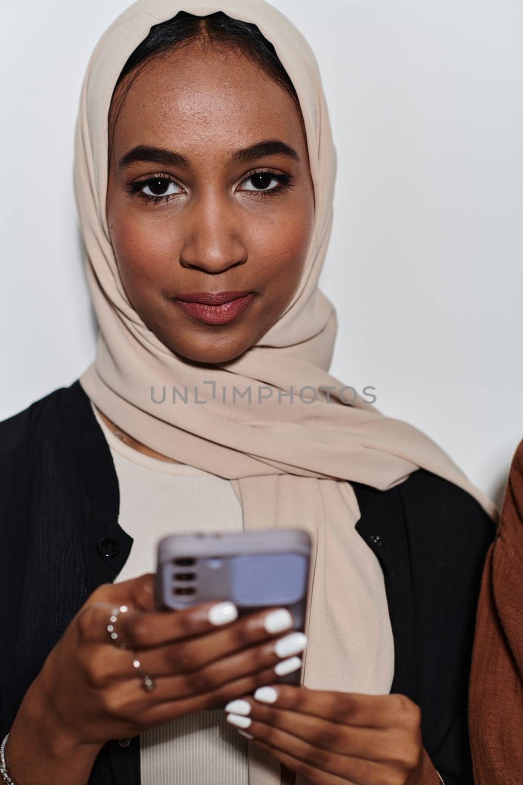 An elegant Arab woman, adorned in a hijab, engages with modernity as she uses a smartphone, the juxtaposition of traditional attire against contemporary technology captured in the isolated setting against a pristine white background by dotshock