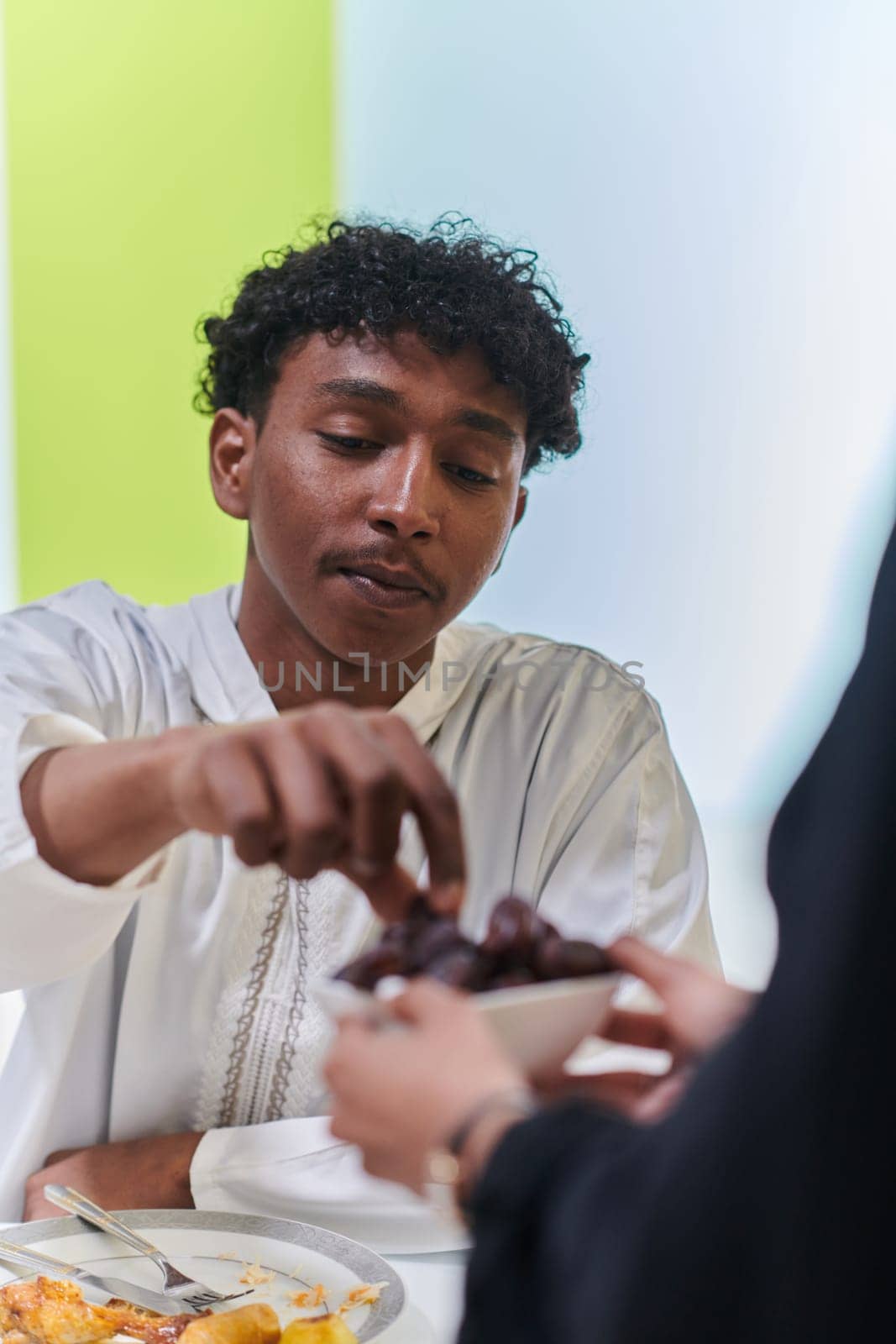 African American Muslim man delicately takes dates to break his fast during the Ramadan month, seated at the family dinner table, embodying a scene of spiritual reflection, cultural tradition, and the shared anticipation of the communal iftar.