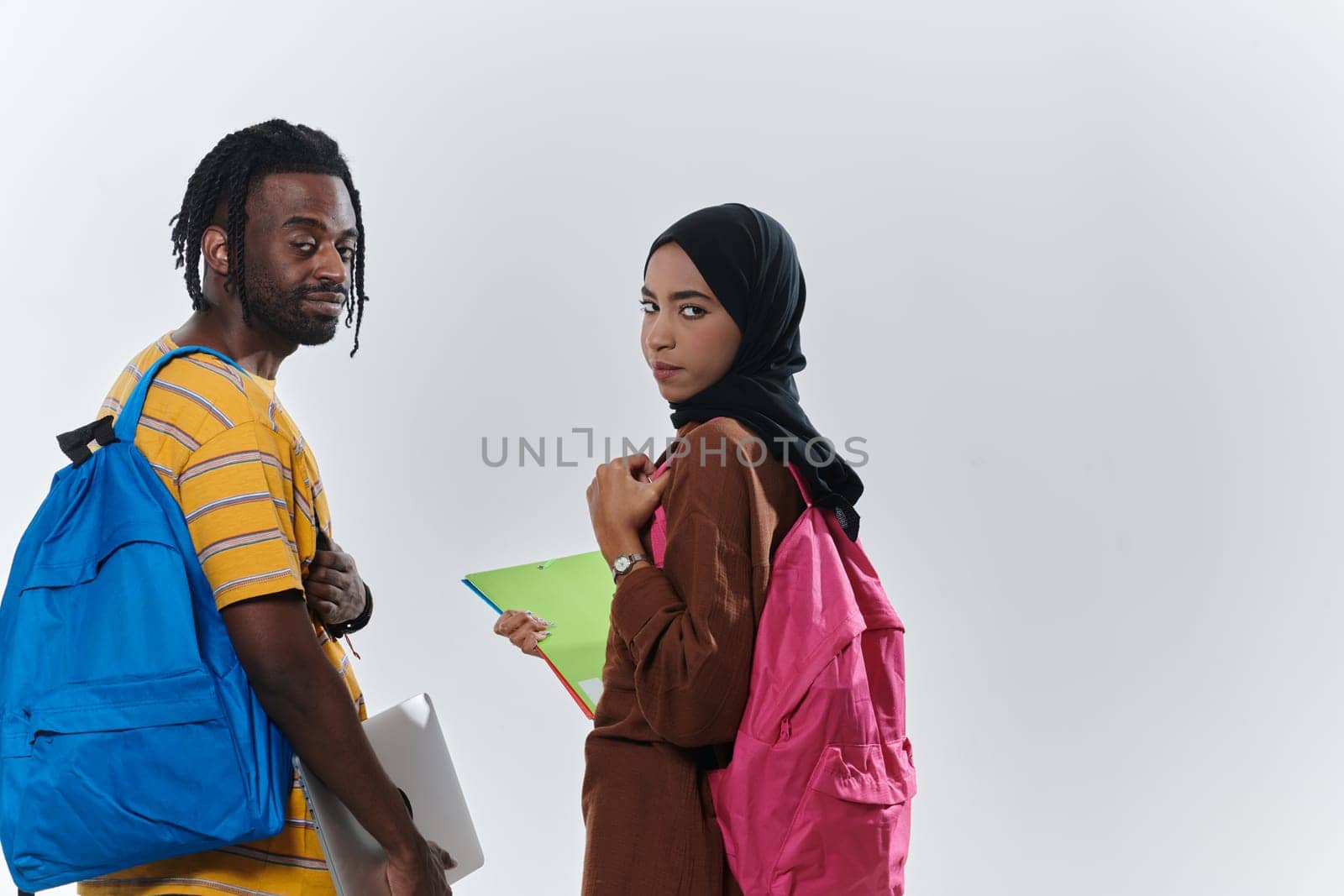 African American student collaborates with his Muslim colleague, who diligently works on her laptop, symbolizing a blend of diversity, modern learning, and cooperative spirit against a serene white background by dotshock