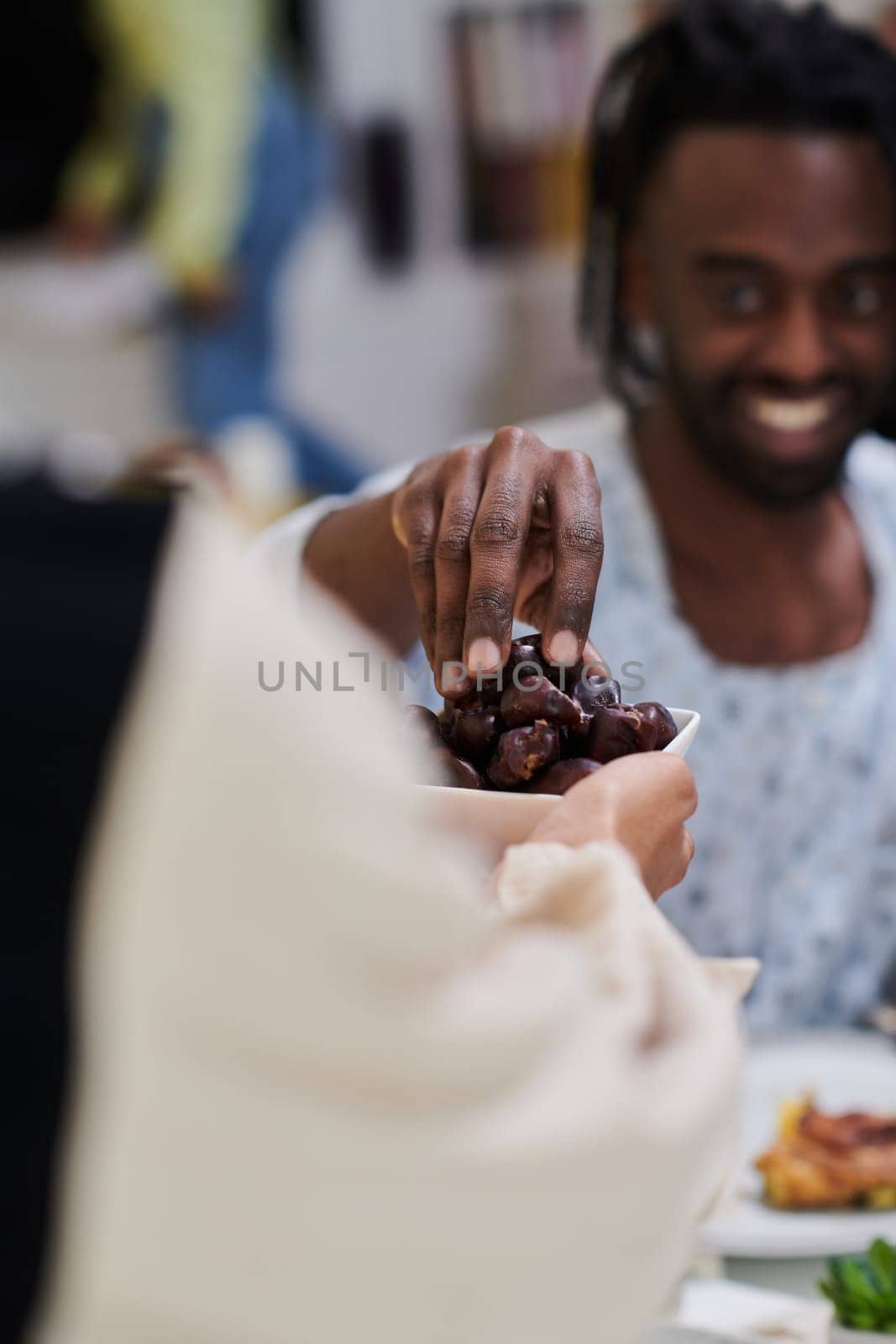 African American Muslim man delicately takes dates to break his fast during the Ramadan month, seated at the family dinner table, embodying a scene of spiritual reflection, cultural tradition, and the shared anticipation of the communal iftar by dotshock