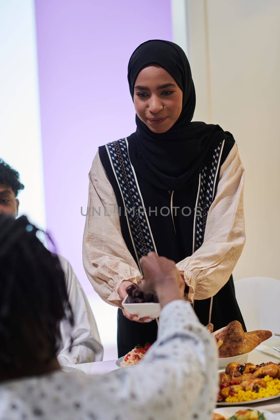 In a heartwarming scene during the sacred month of Ramadan, a traditional Muslim woman offers dates to her family gathered around the table, exemplifying the spirit of unity, generosity, and cultural richness during this festive and spiritual occasion.