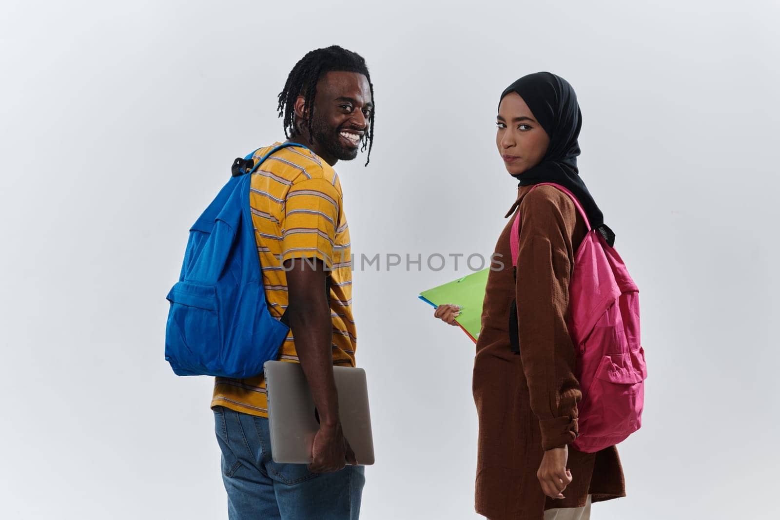 African American student collaborates with his Muslim colleague, who diligently works on her laptop, symbolizing a blend of diversity, modern learning, and cooperative spirit against a serene white background.