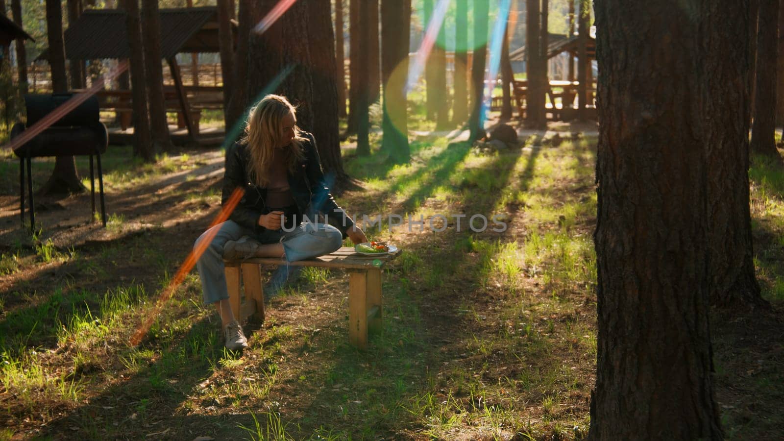 Girl sitting on picnic bench in green park near camp among trees. Stock footage. Woman spending time alone outdoors