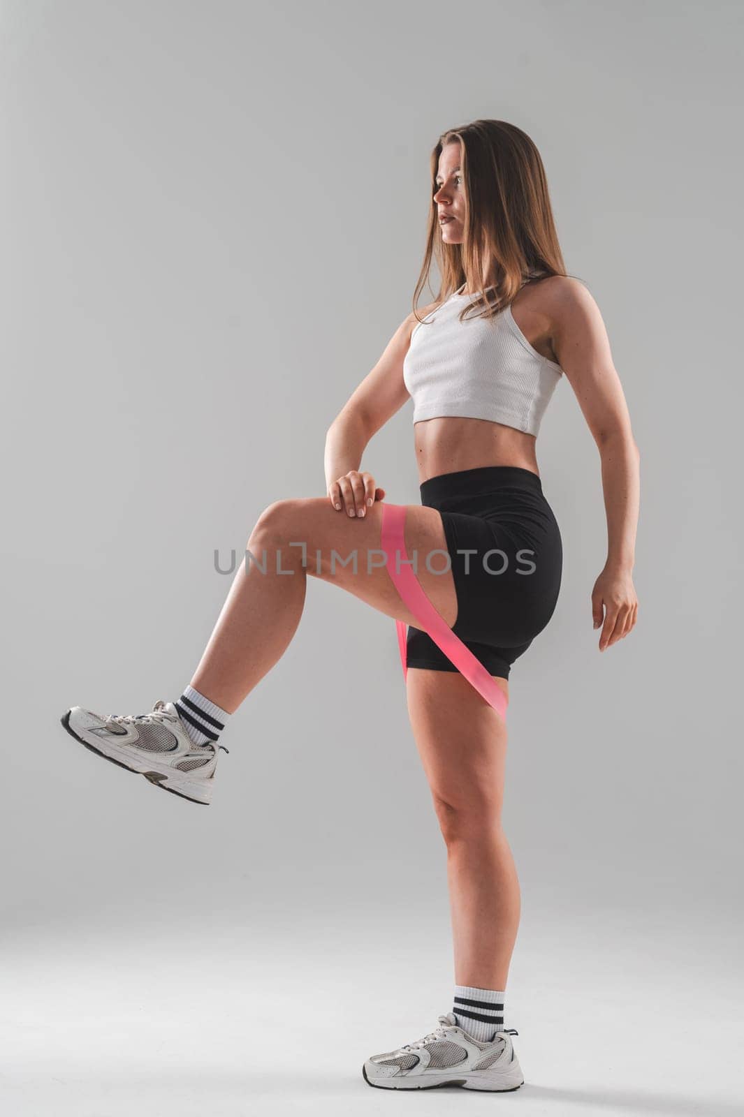 Caucasian woman doing exercises with a fitness elastic band on a white background. Vertical photo