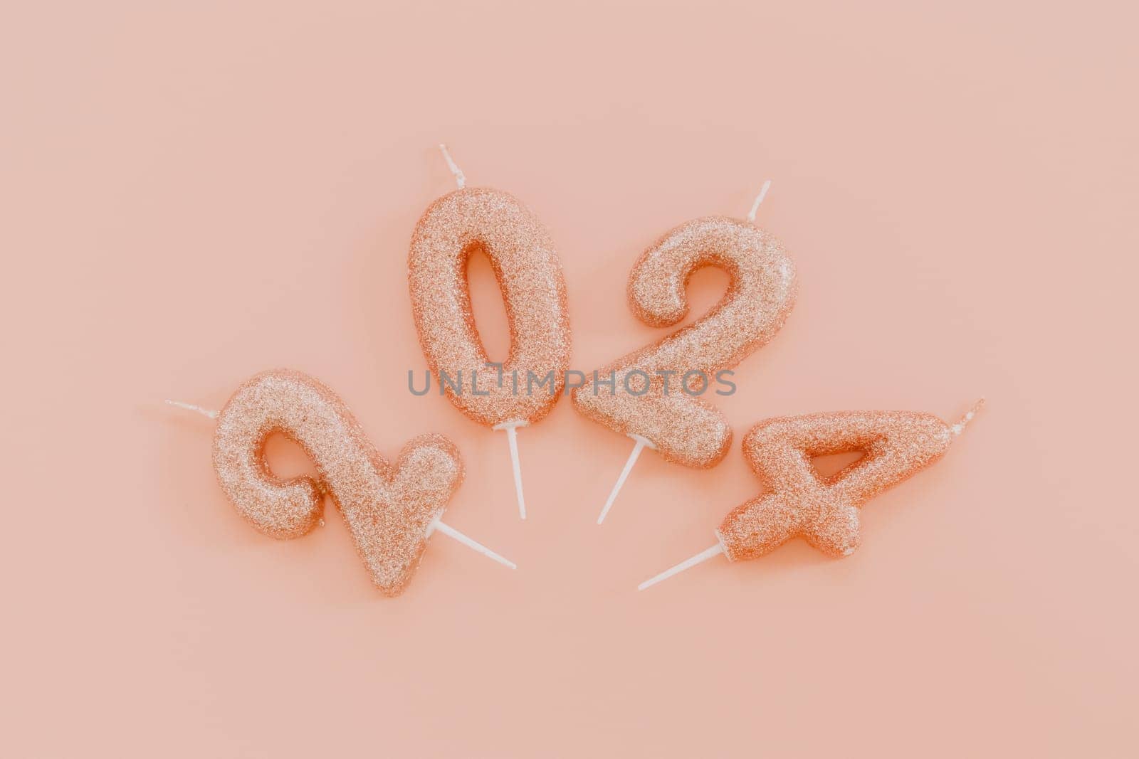 Shiny candle numbers 2024 lie in a semicircle in the center on a pink background, flat lay close-up.