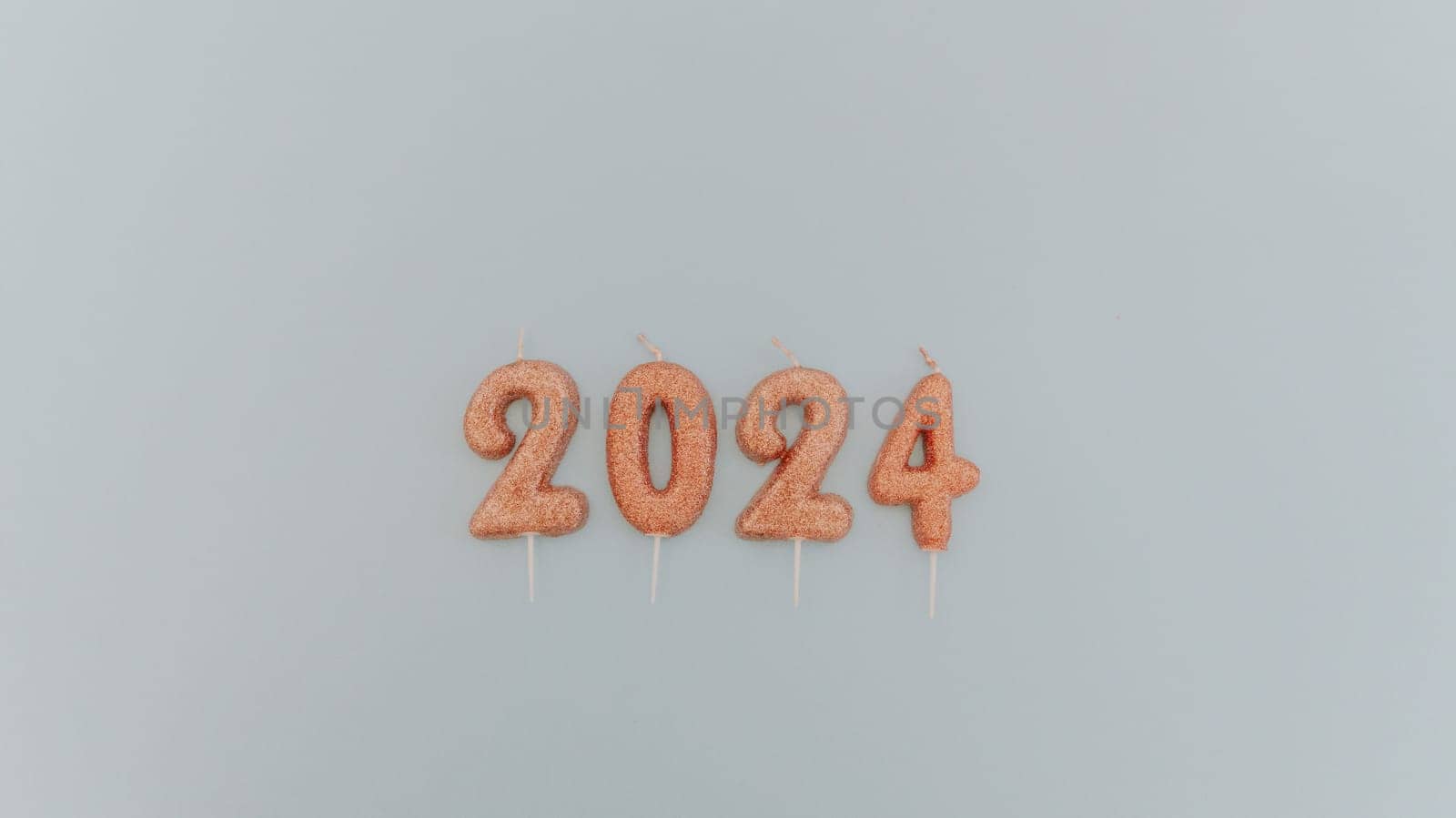 Shiny light brown candles number 2024 lie in the center on a pastel blue background with copy space on the sides, flat lay close-up.