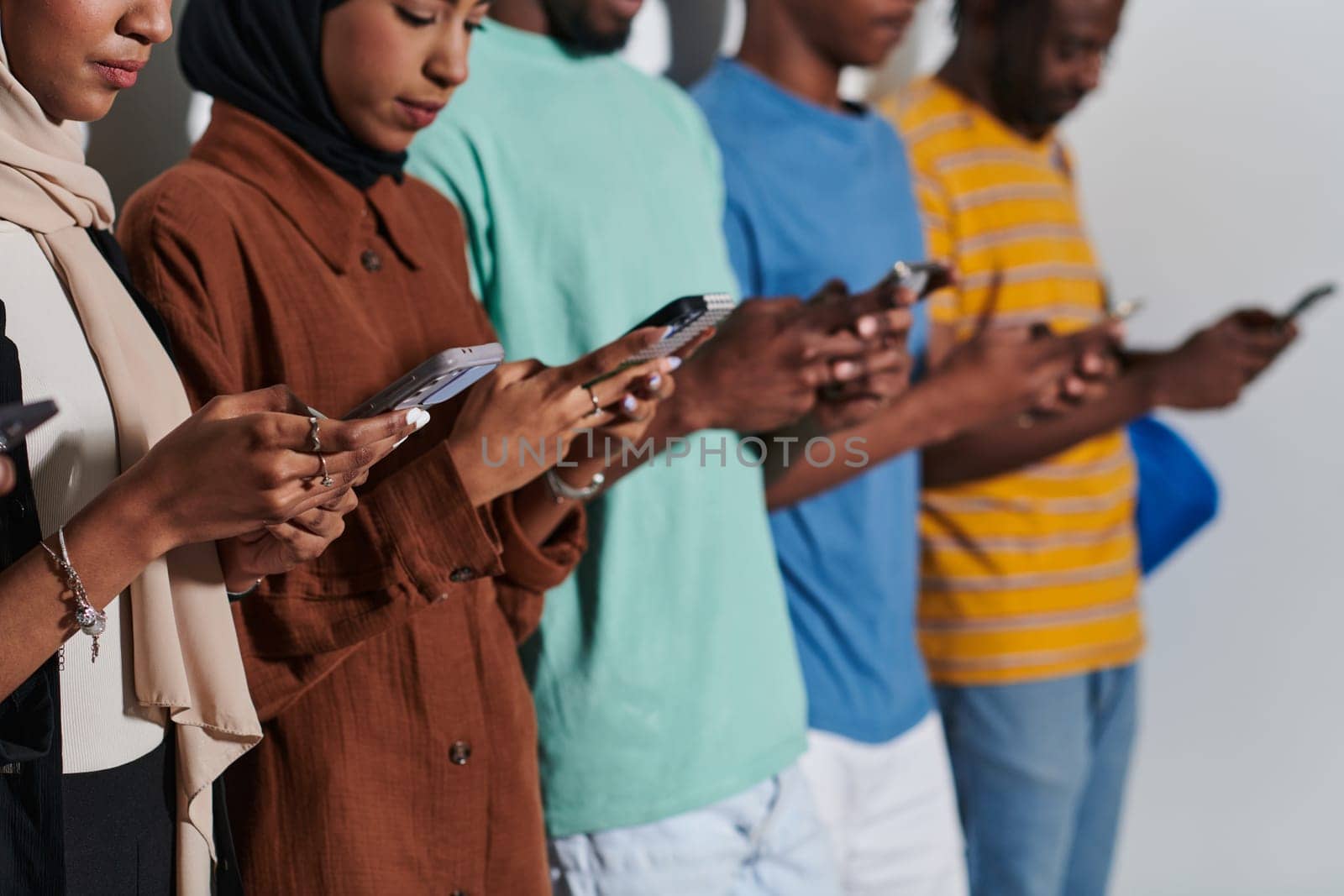 A diverse group of students, immersed in the digital age, stands united while engaging with their smartphones against a white backdrop, symbolizing the modern era of connectivity, communication, and collaborative learning.