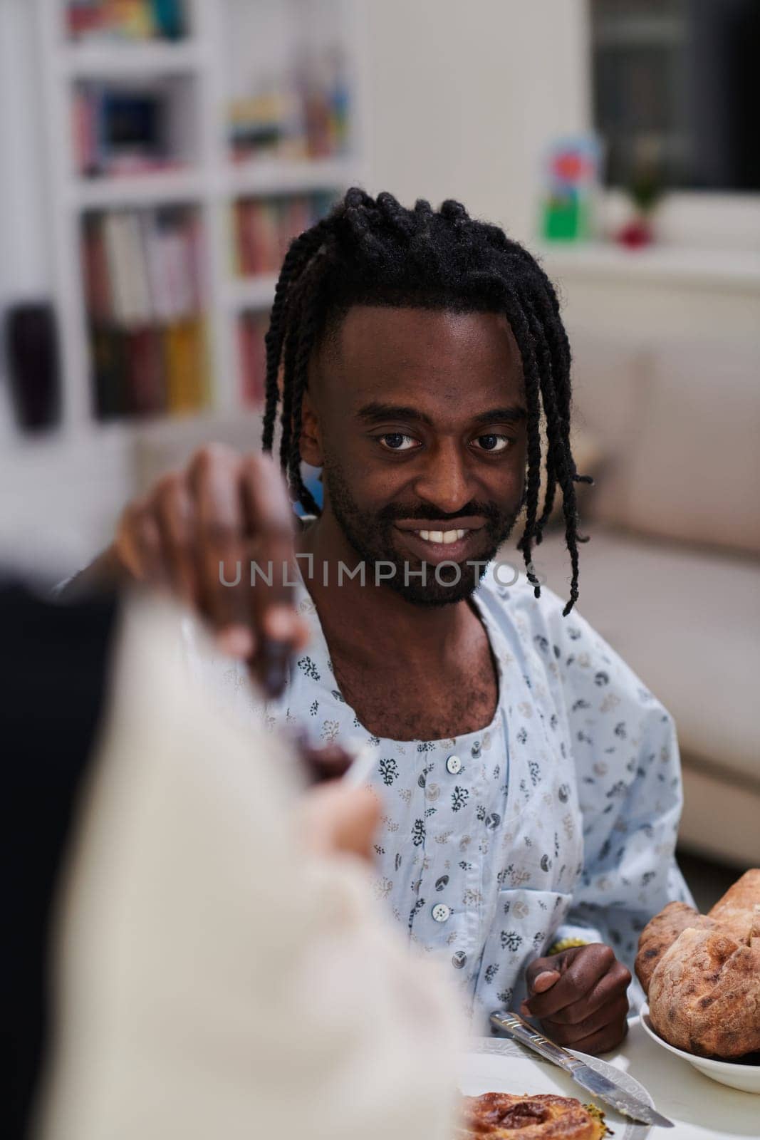 African American Muslim man delicately takes dates to break his fast during the Ramadan month, seated at the family dinner table, embodying a scene of spiritual reflection, cultural tradition, and the shared anticipation of the communal iftar by dotshock