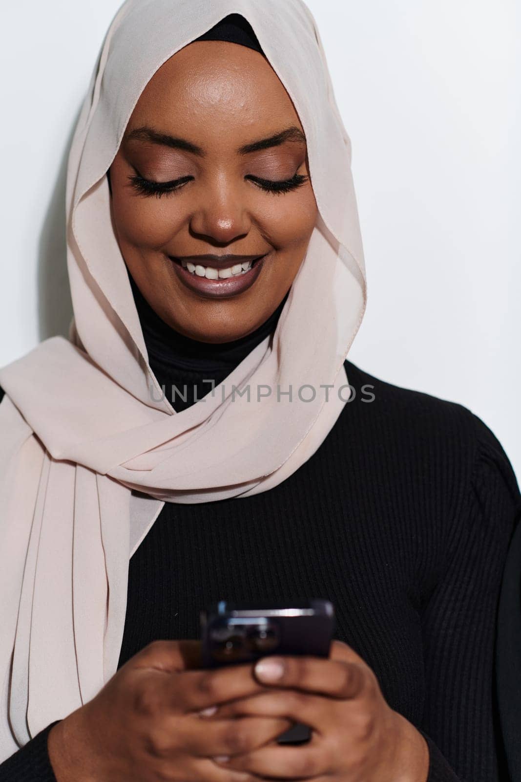 An elegant Arab woman, adorned in a hijab, engages with modernity as she uses a smartphone, the juxtaposition of traditional attire against contemporary technology captured in the isolated setting against a pristine white background.