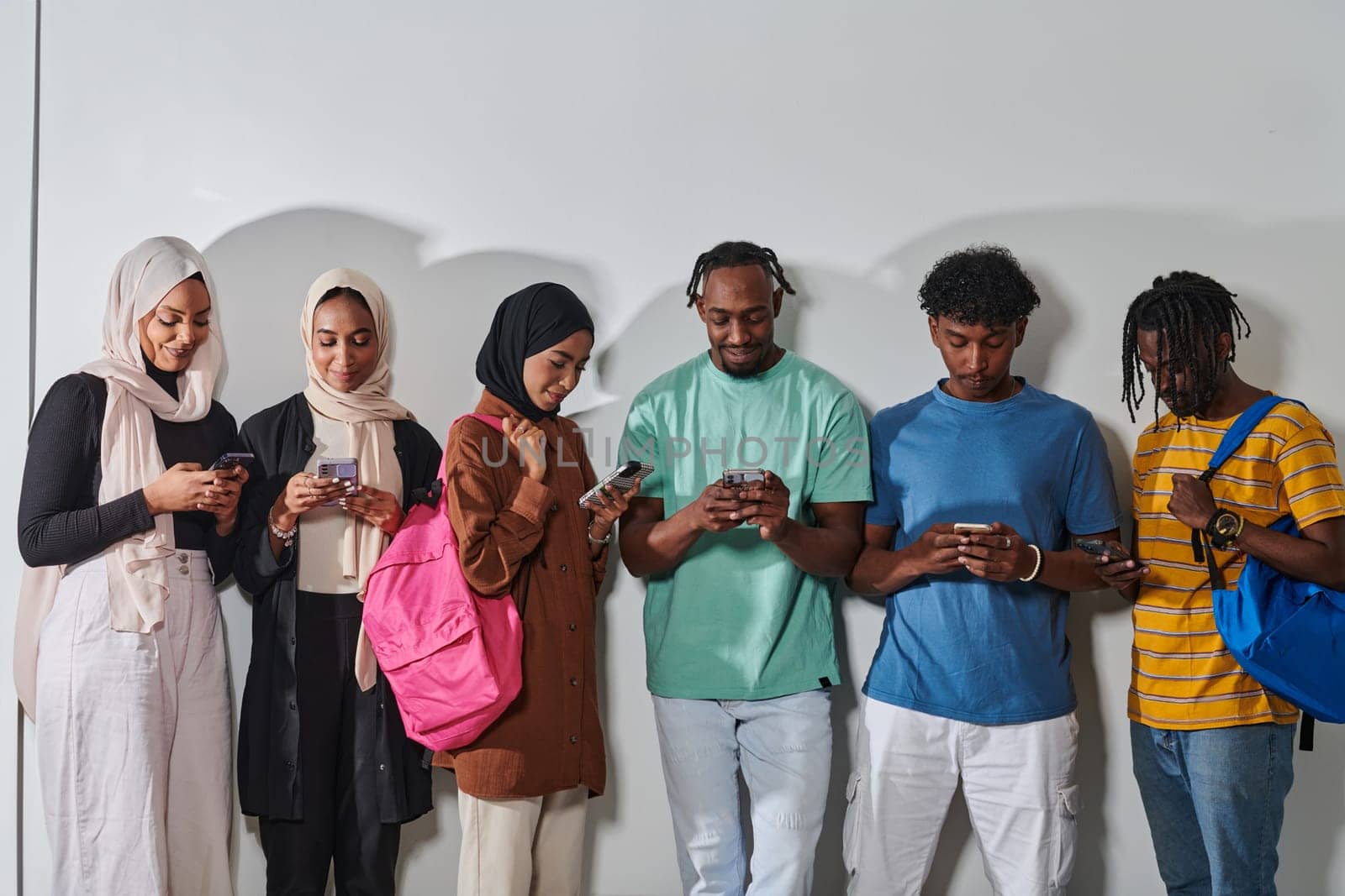 A diverse group of students, immersed in the digital age, stands united while engaging with their smartphones against a white backdrop, symbolizing the modern era of connectivity, communication, and collaborative learning.