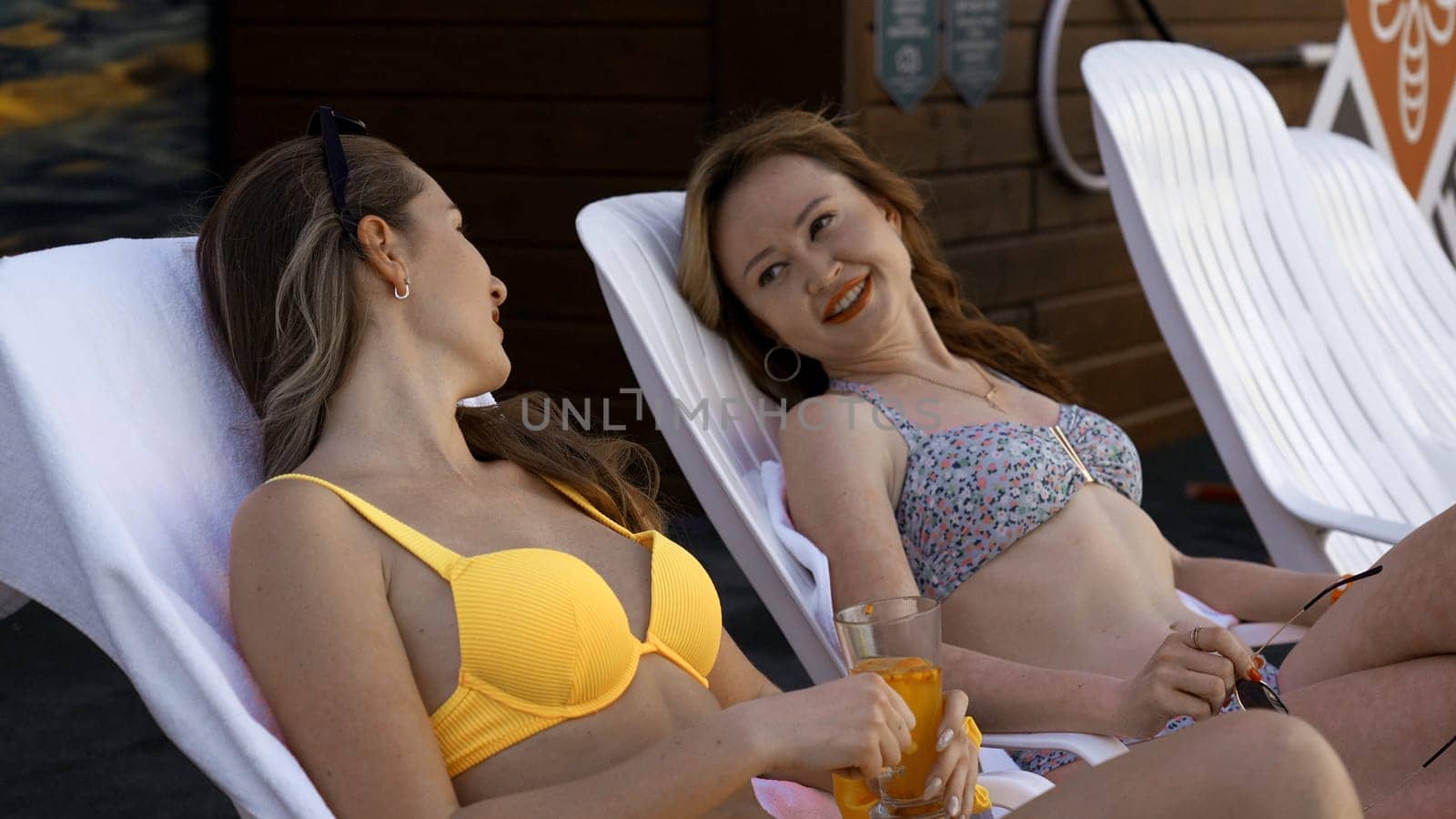 Young caucasian girls relaxing by the hotel pool. Clip. Adult women gossiping and smiling during vacation