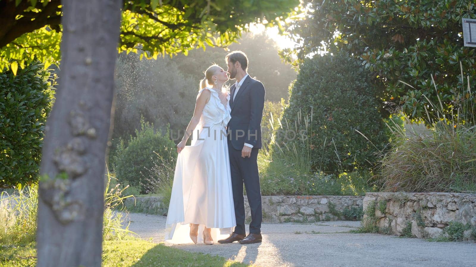 Photo shoot of the bride and groom. Action.The newlyweds are photographed in different places,some posing in the park on the street under the sun,the second on the white staircase,looking at each other tenderly. by Mediawhalestock